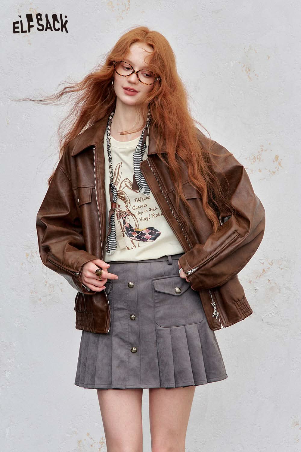 ELFSACK bunny graphic tee for women paired with a brown leather jacket and gray pleated skirt