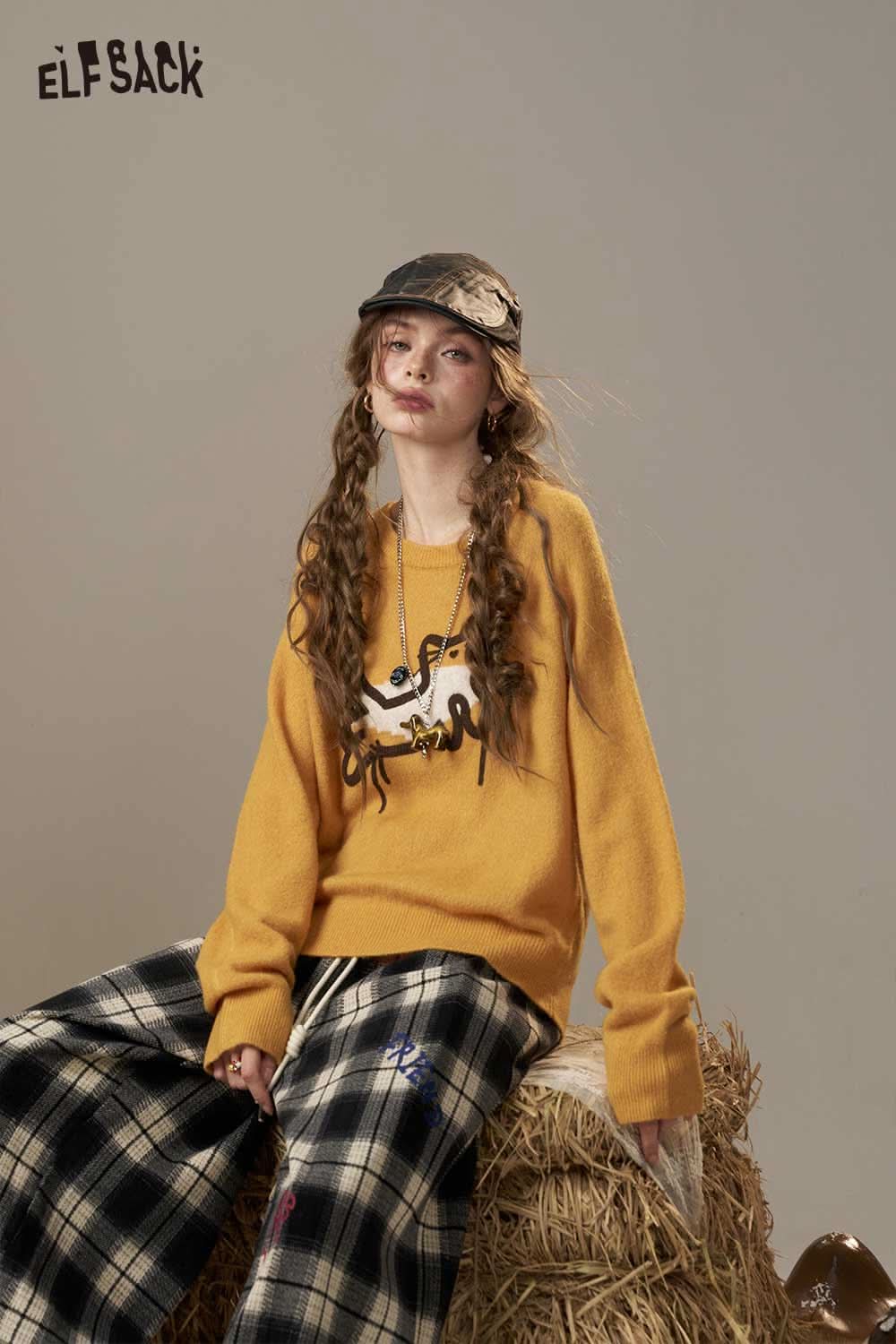 ELFSACK cartoon embroidery sweater in mustard yellow with playful design, styled with plaid pants