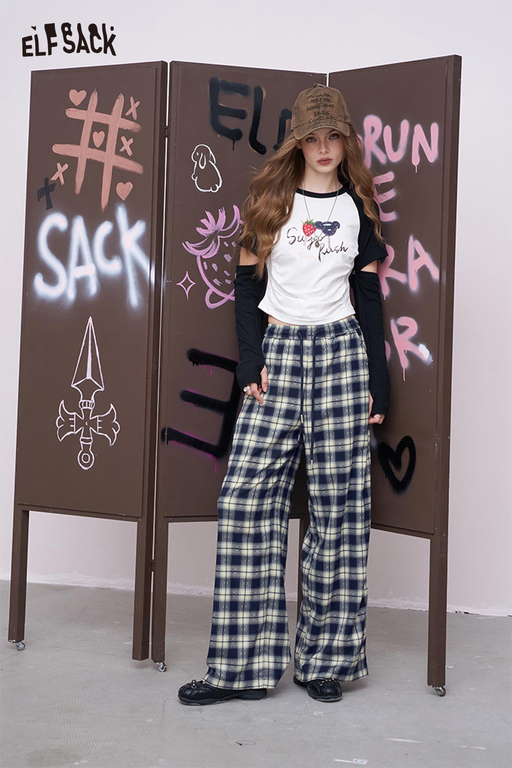 ELFSACK model wearing women's plaid wide leg pants in navy cream plaid with white graphic tee and cap