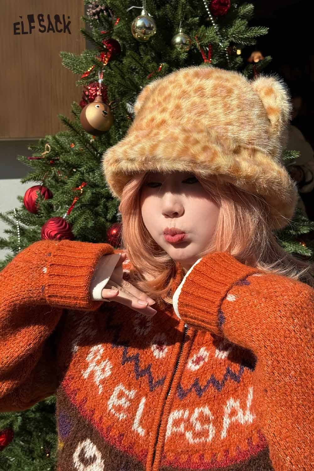 ELFSACK cat ear leopard plush hat in soft fabric, styled with an orange knitted sweater, festive background