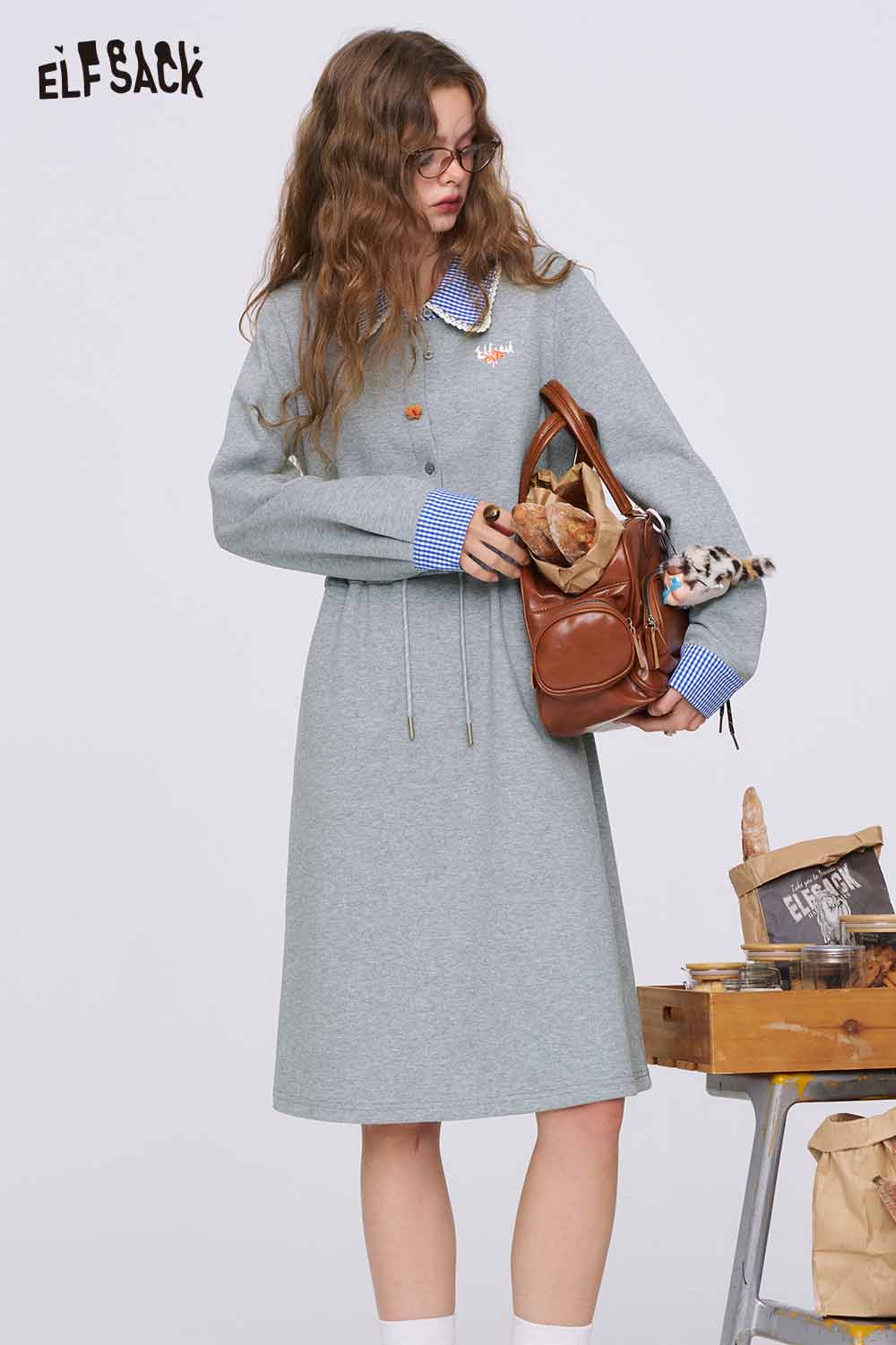 ELFSACK model wearing gray cinched waist dress for women with blue gingham collar and brown tote bag