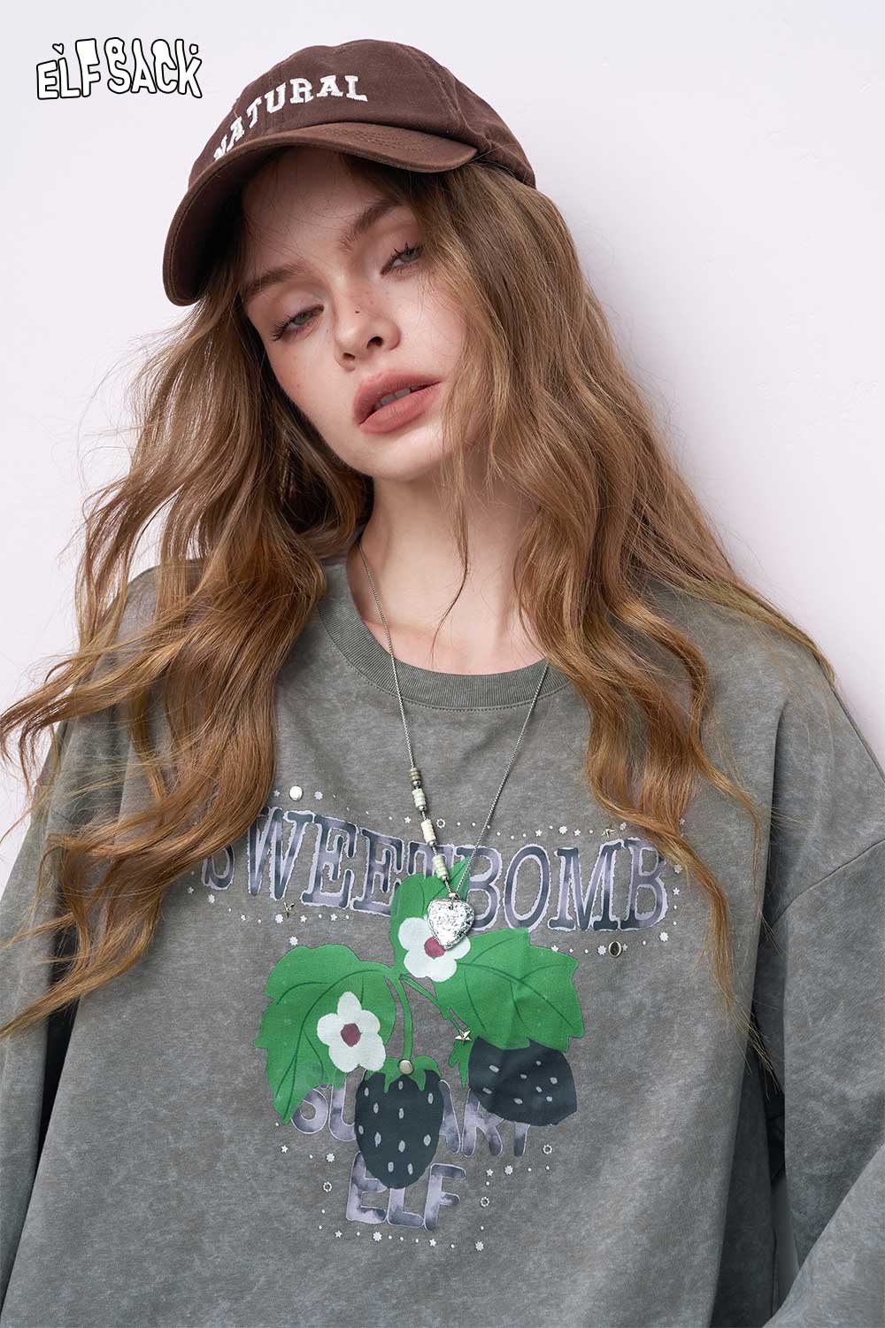 Model wearing ELFSACK embroidered hoodie dress set in faded green with plant graphic sweatshirt dress and brown cap