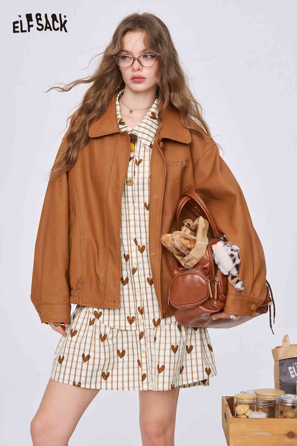 ELFSACK model wearing college style heart plaid dress cream plaid with brown hearts under oversized tan jacket holding brown bag