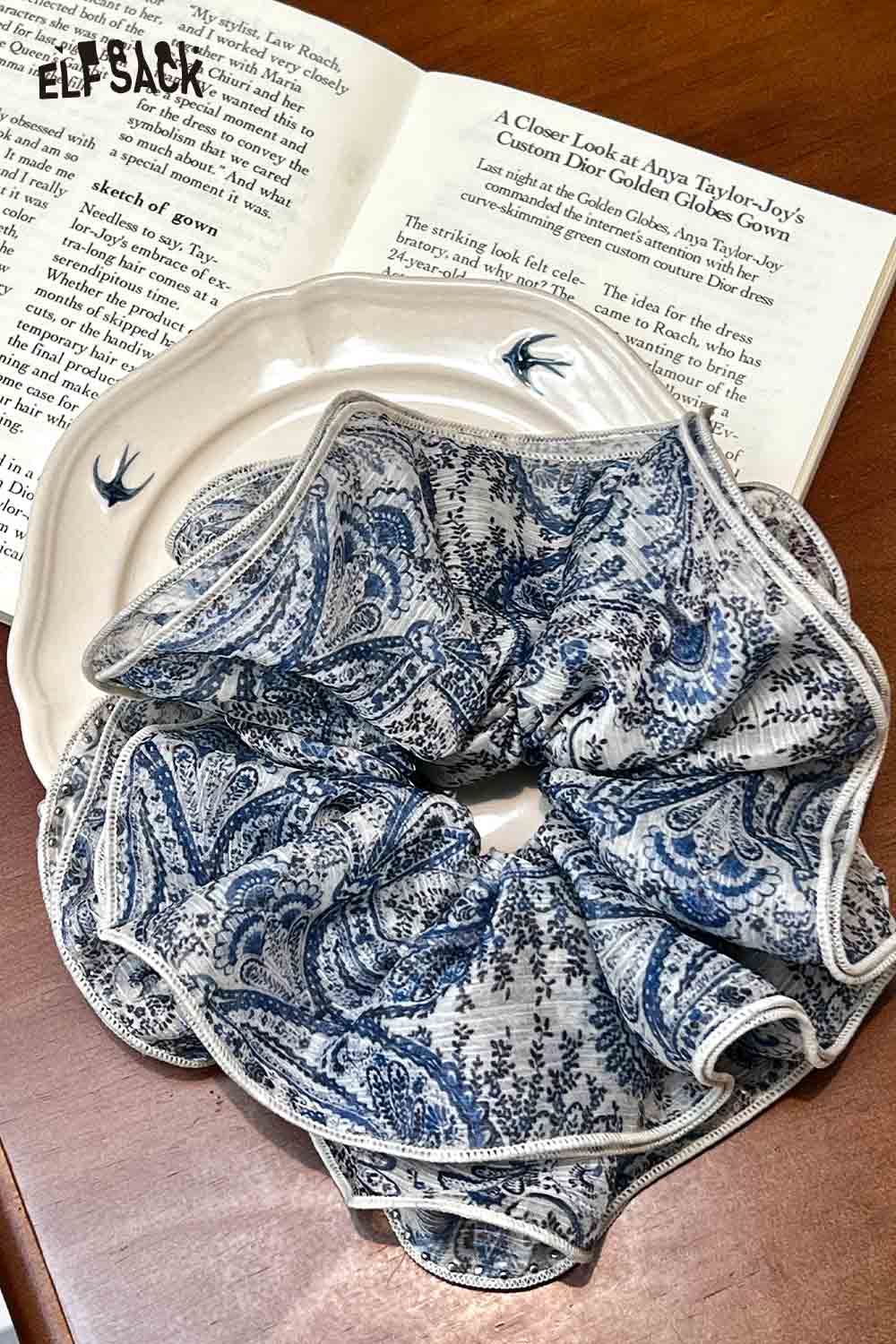 ELFSACK blue and white fabric scrunchie with intricate paisley print on plate and book background bohemian paisley hair tie