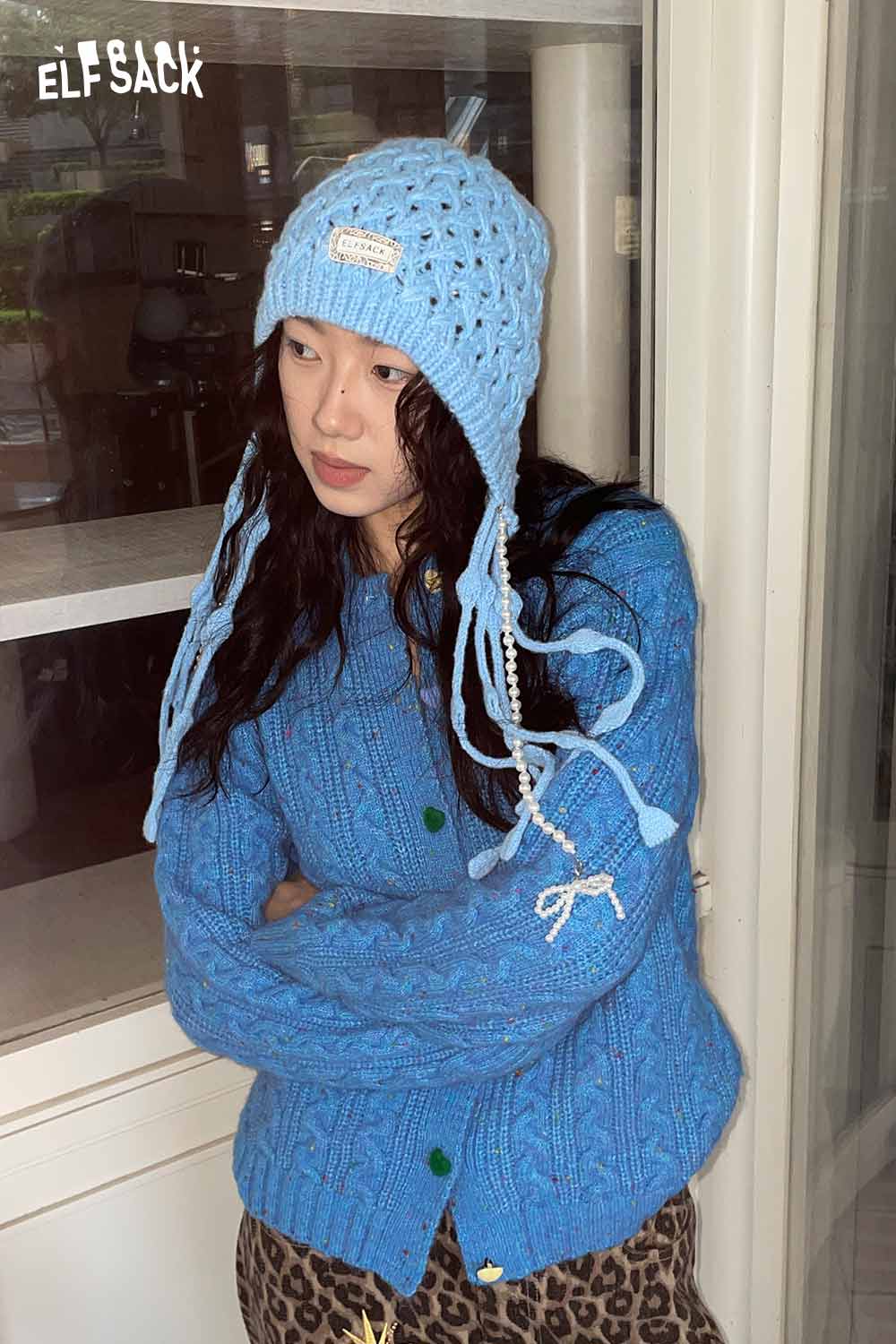 Light blue crocheted tassel ear-flap hat with long ties paired with a cozy sweater for stylish warmth