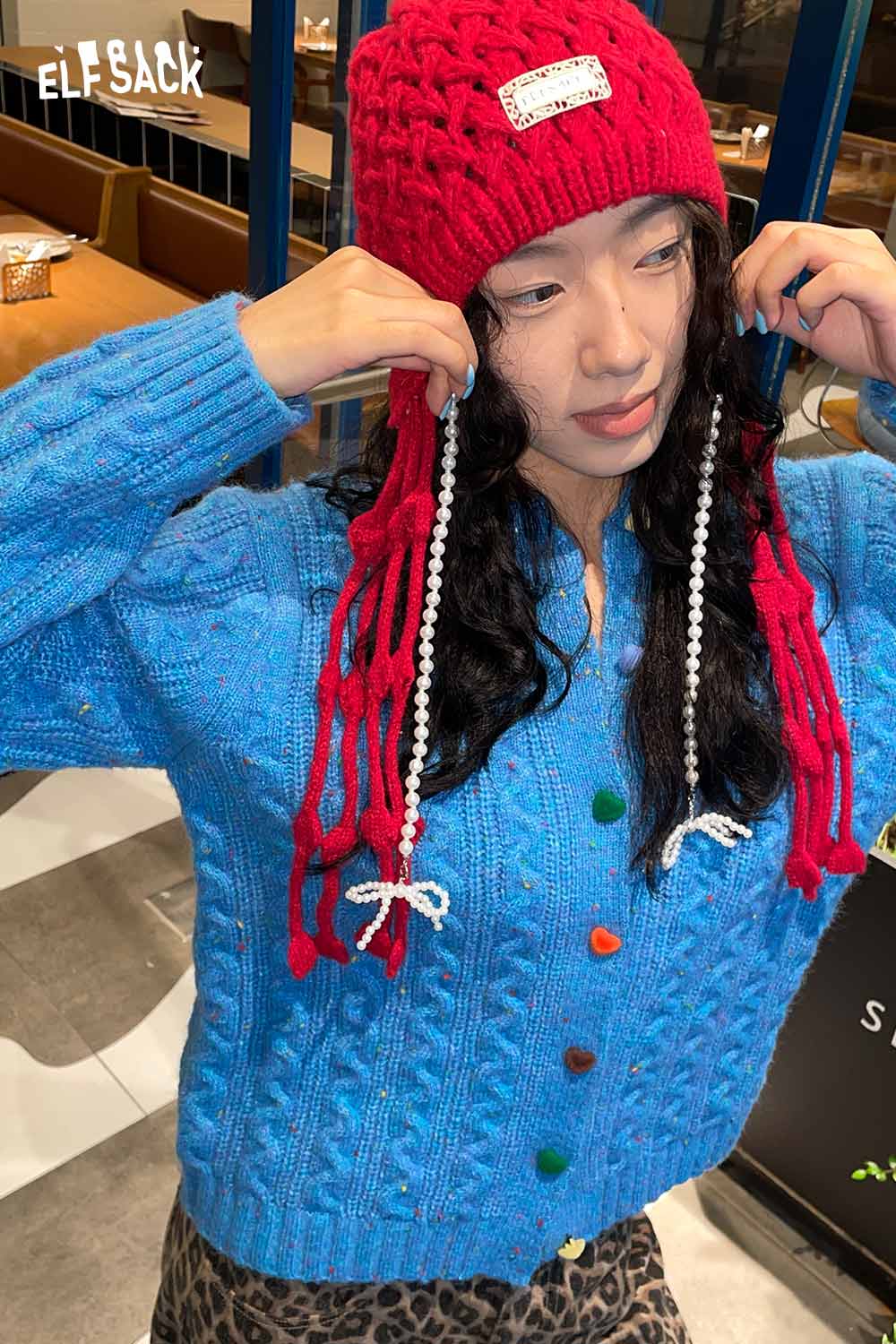 ELFSACK crocheted tassel ear-flap hat in red paired with a cozy blue cardigan
