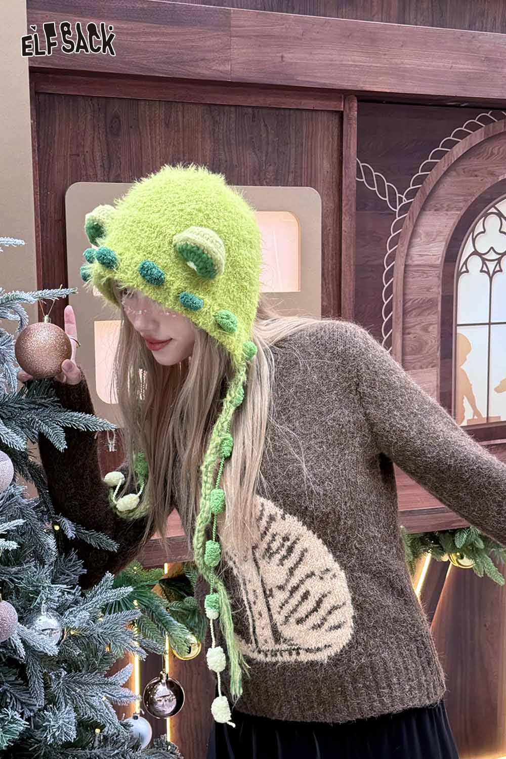 Model wearing a cute 3D ear beanie hat with green accents and a cozy sweater in a festive setting