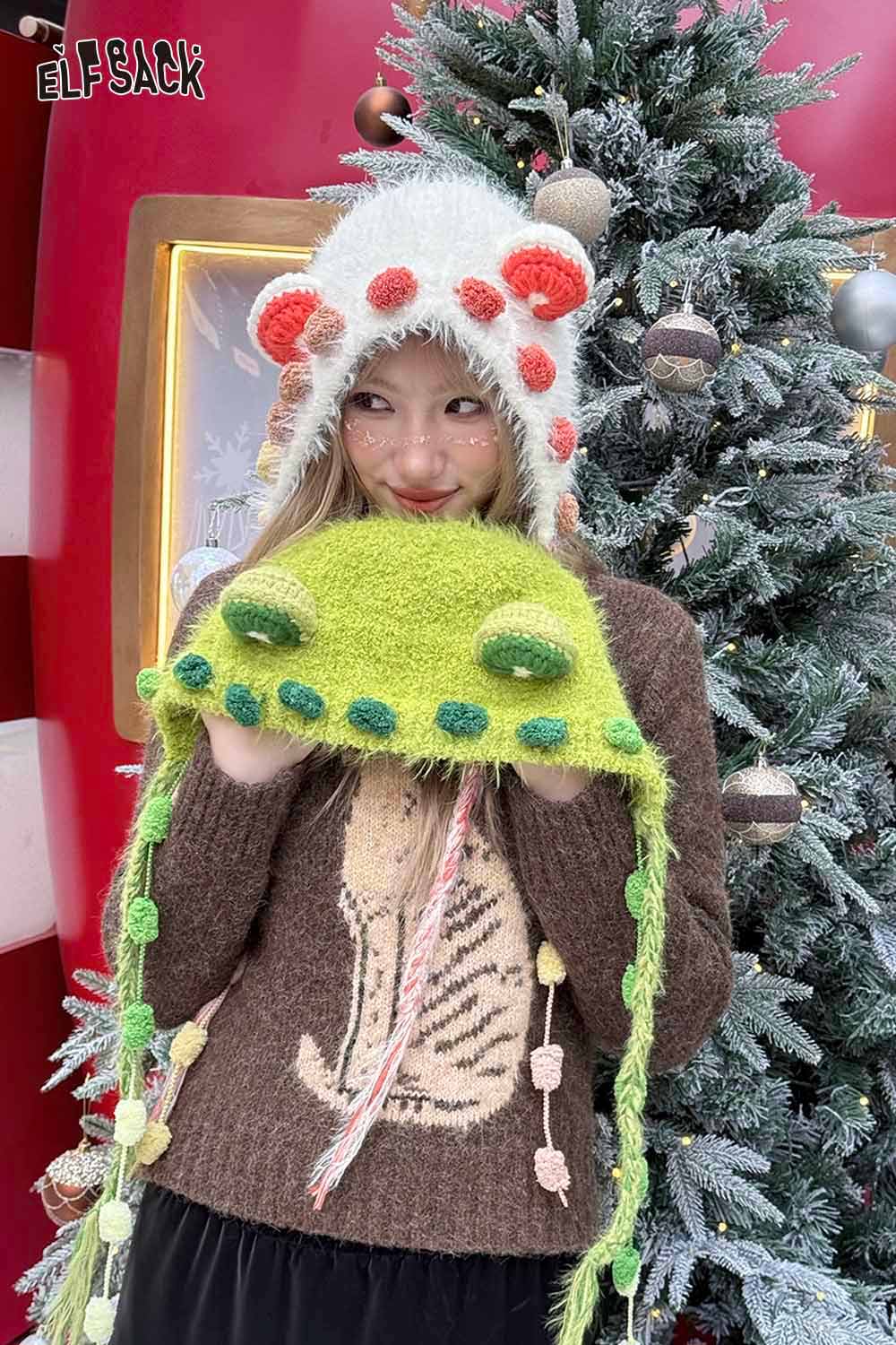 Girl wearing a cute 3D ear beanie hat and holding a green fuzzy hat with animal features