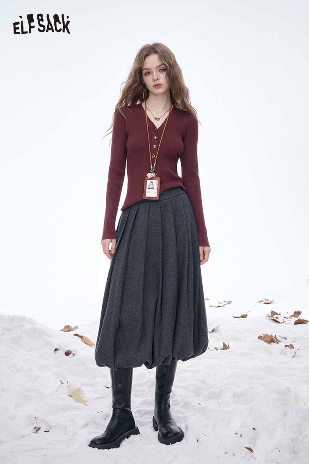 Model wearing a dark gray pleated half skirt paired with a burgundy top and stylish black boots