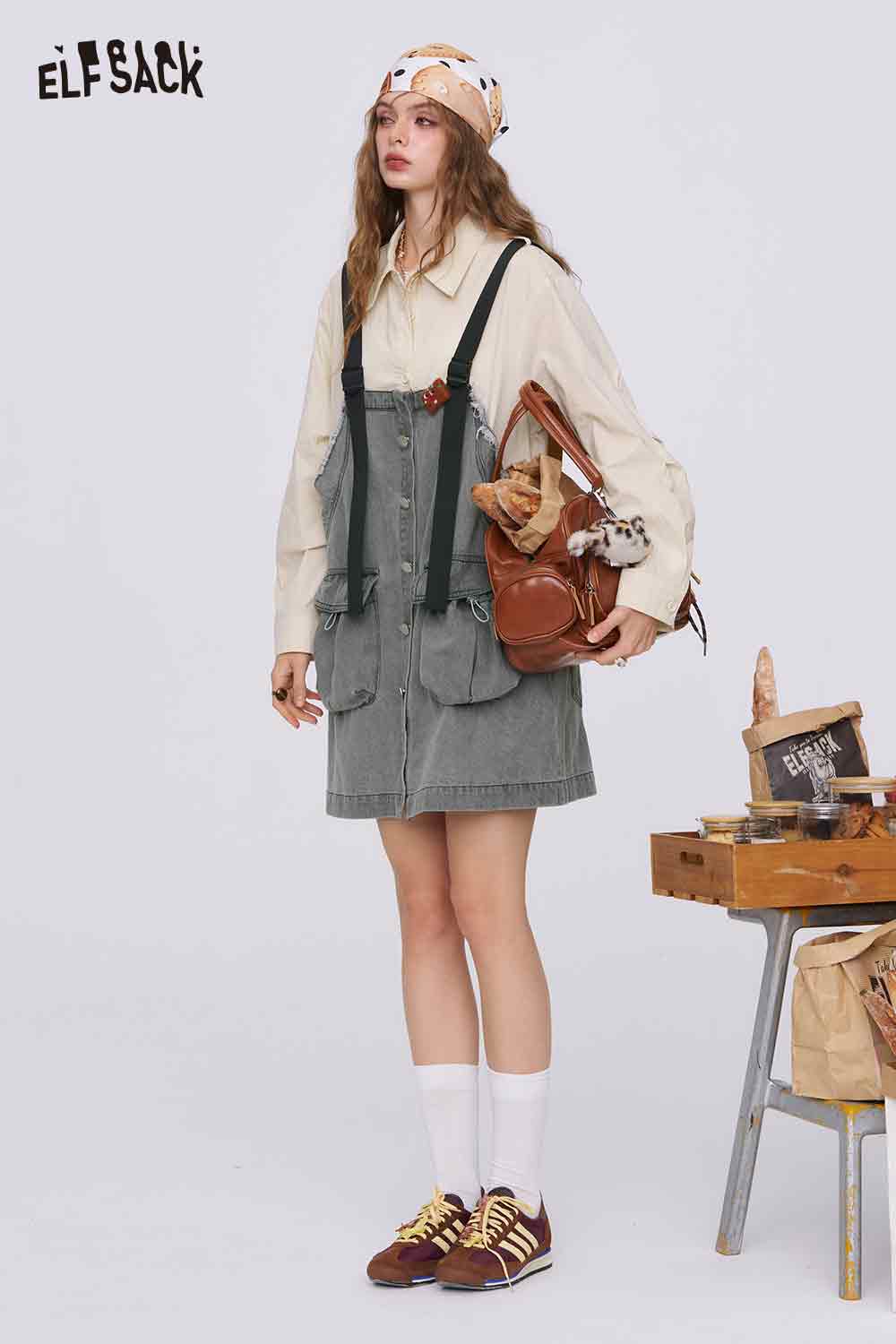ELFSACK model wearing denim color-block midi dress layered over oversized cream blouse with brown satchel and sneakers