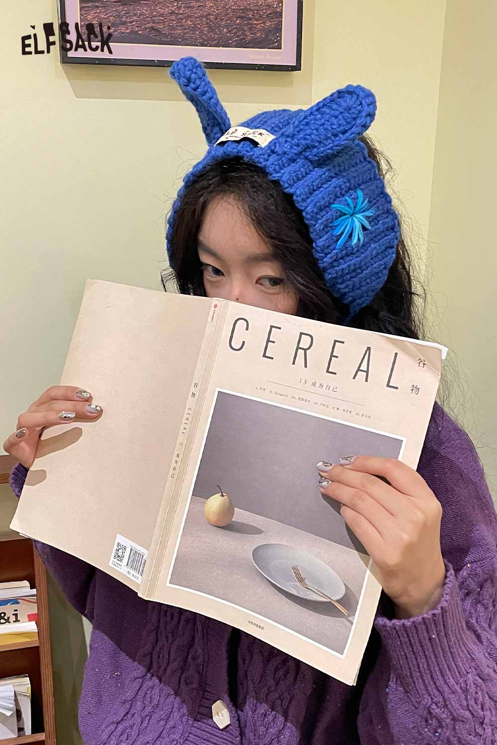 ELFSACK 3D bunny ear knit ear warmers in blue, adding cozy style while reading a magazine