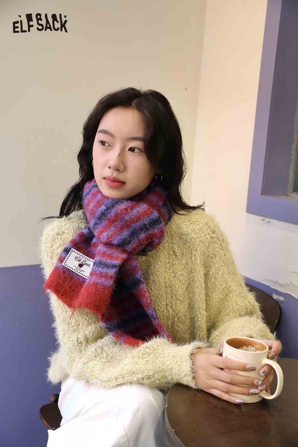 Cozy woman wearing a Christmas striped scarf for women, enjoying a warm drink indoors