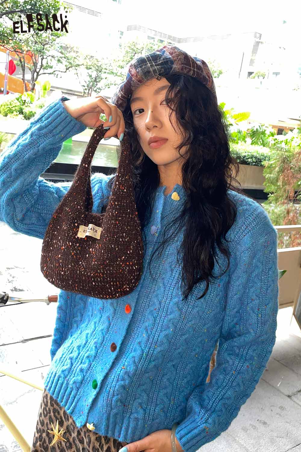 Fashionable model holding a color block handwoven tote bag paired with a cozy blue cardigan