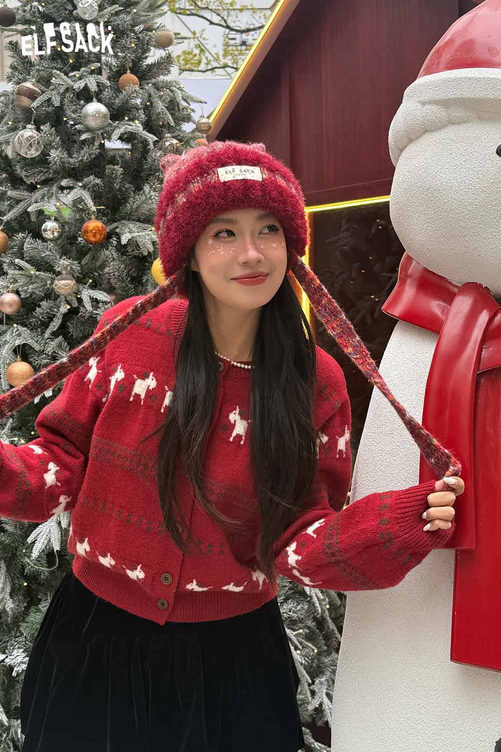 Cozy ELFSACK cute cat ear beanie for women paired with a festive red cardigan and snowman backdrop