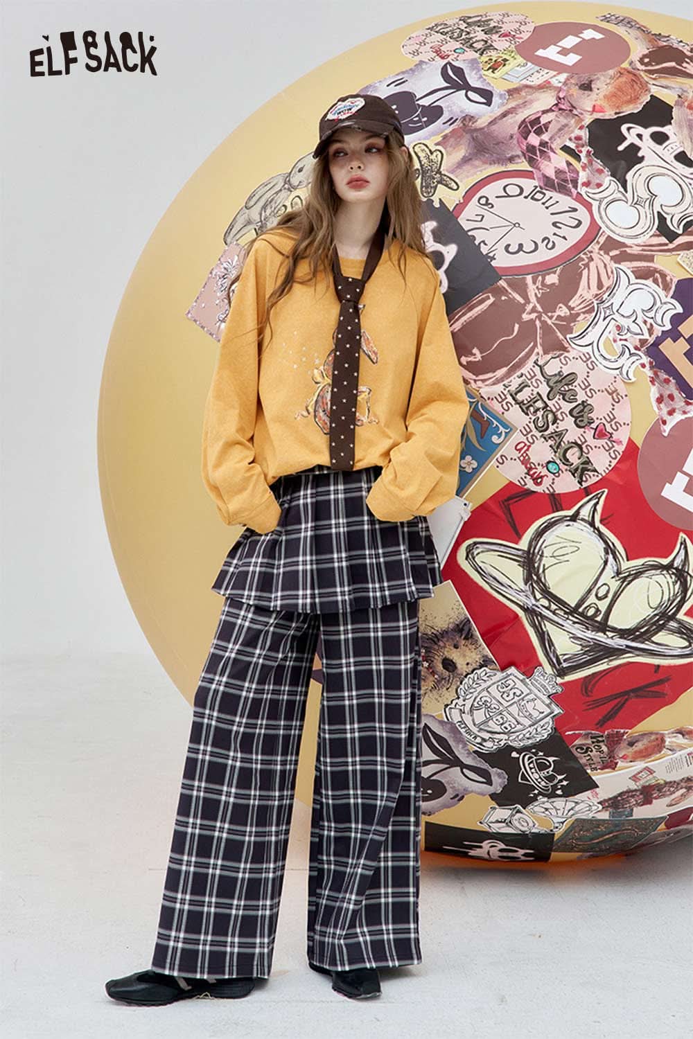 ELFSACK organic cotton embroidered long sleeve tee in mustard color, styled with plaid trousers and a cap