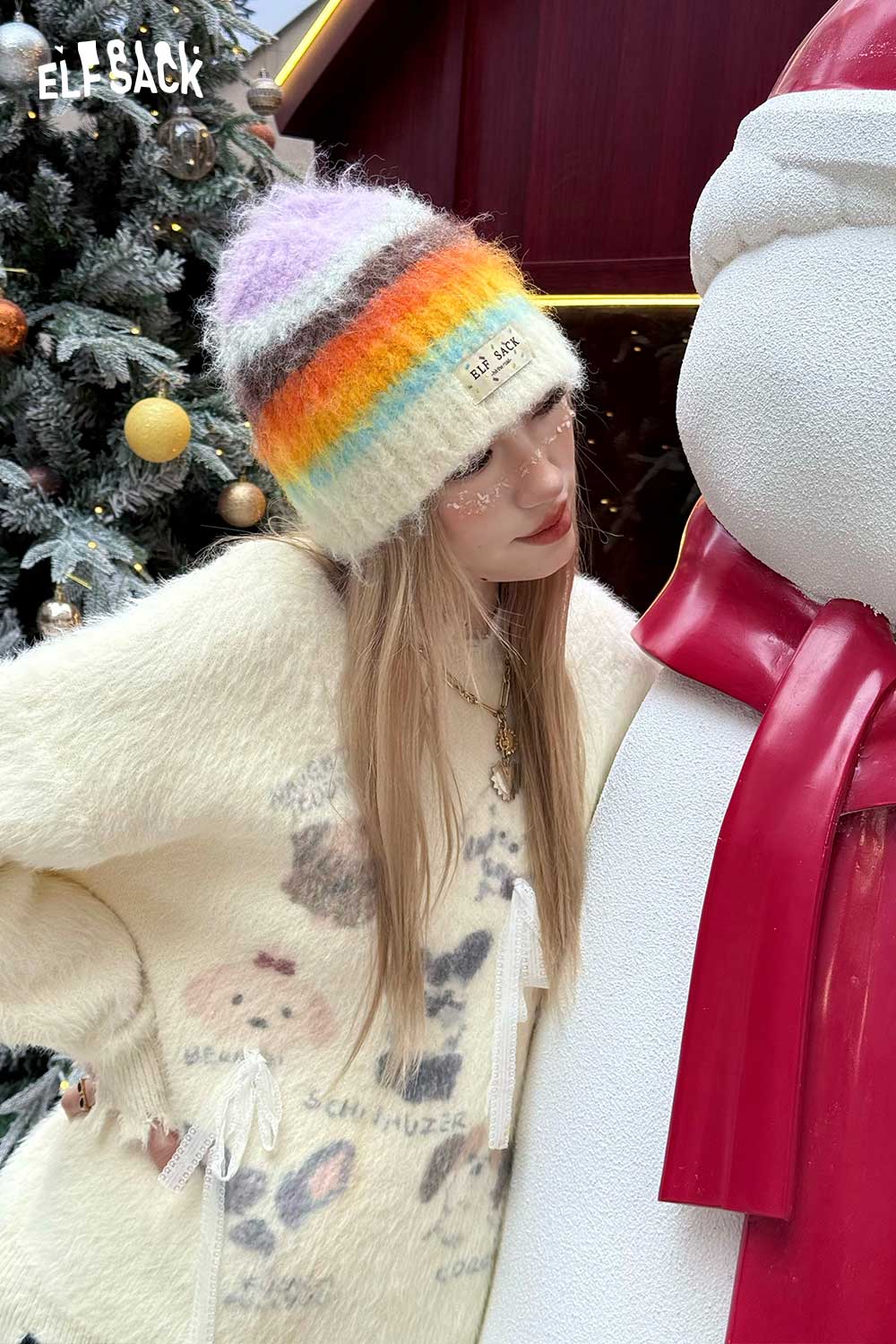 ELFSACK rainbow striped knit beanie worn by a model with a cozy outfit in a festive setting