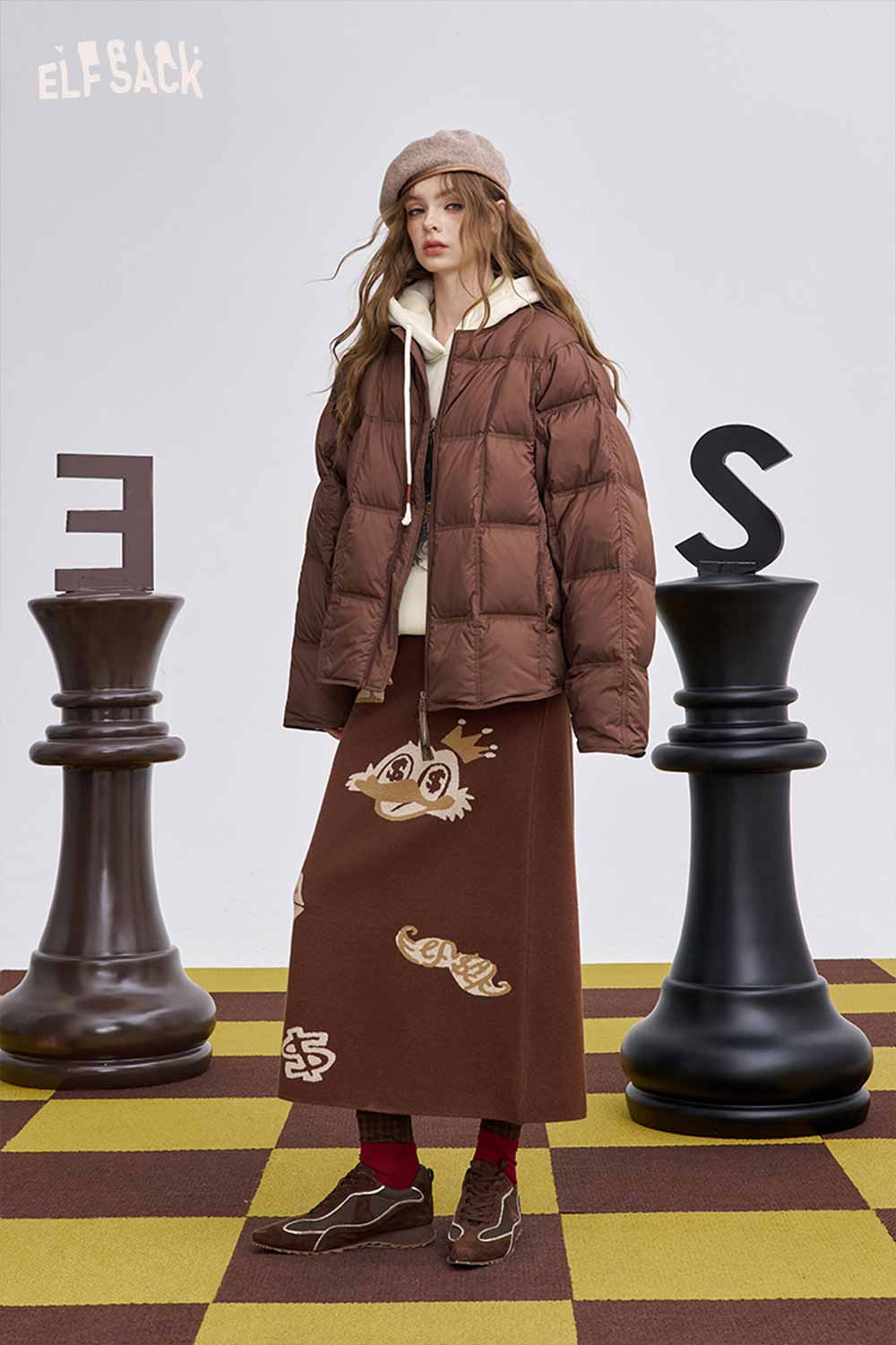 ELFSACK soft graphic hooded sweatshirt paired with a stylish puffer jacket and brown skirt in a chess-themed setting