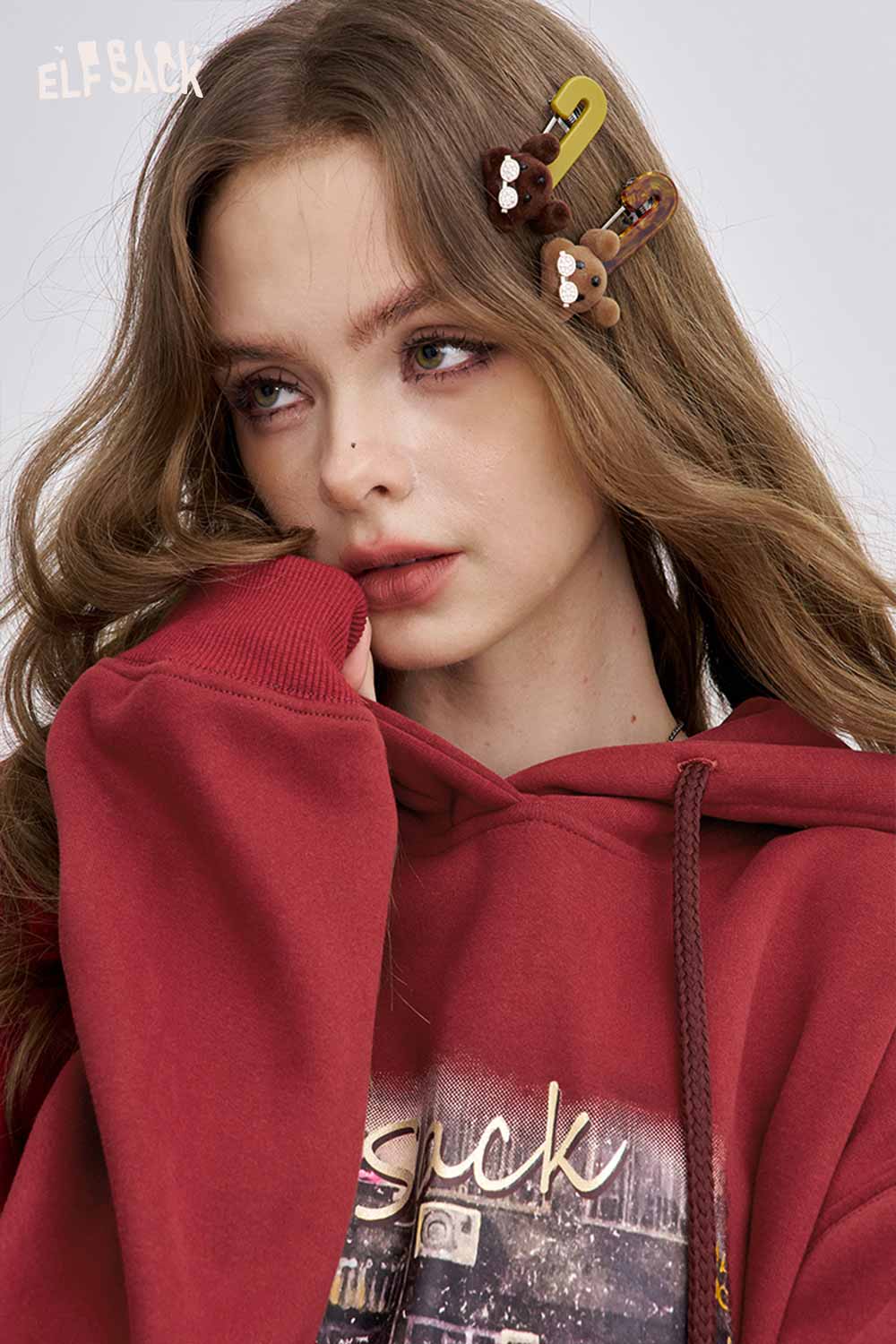 Model wearing a soft graphic hooded sweatshirt in burgundy with playful accessories in her hair