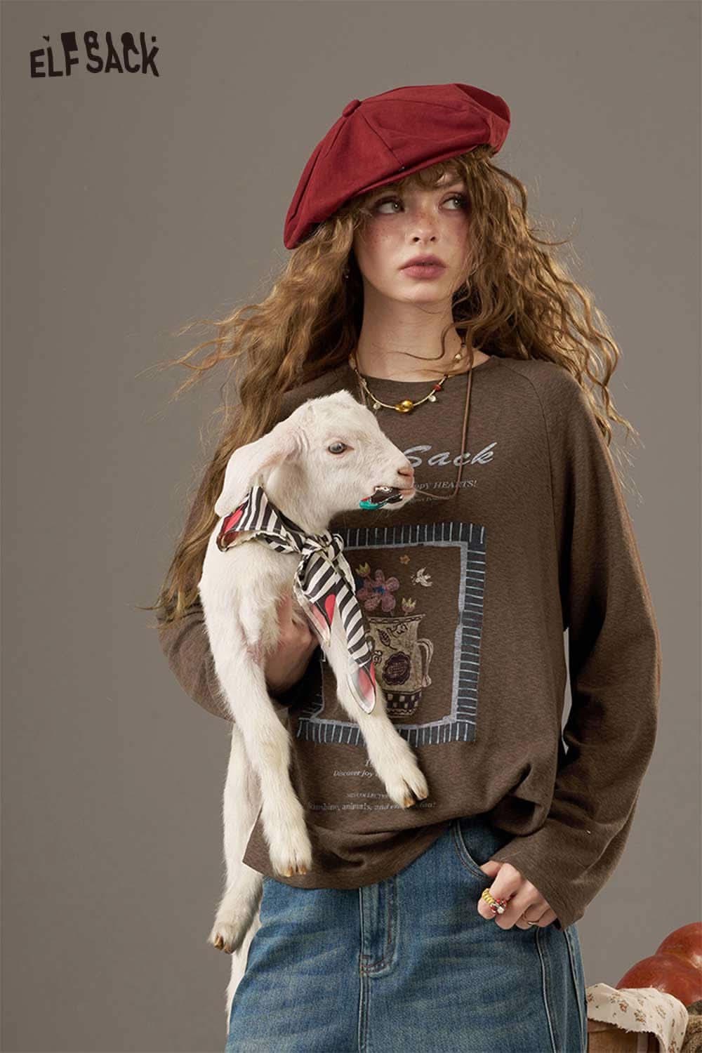 ELFSACK soft printed raglan sleeve sweatshirt in brown, styled with a model holding a baby goat
