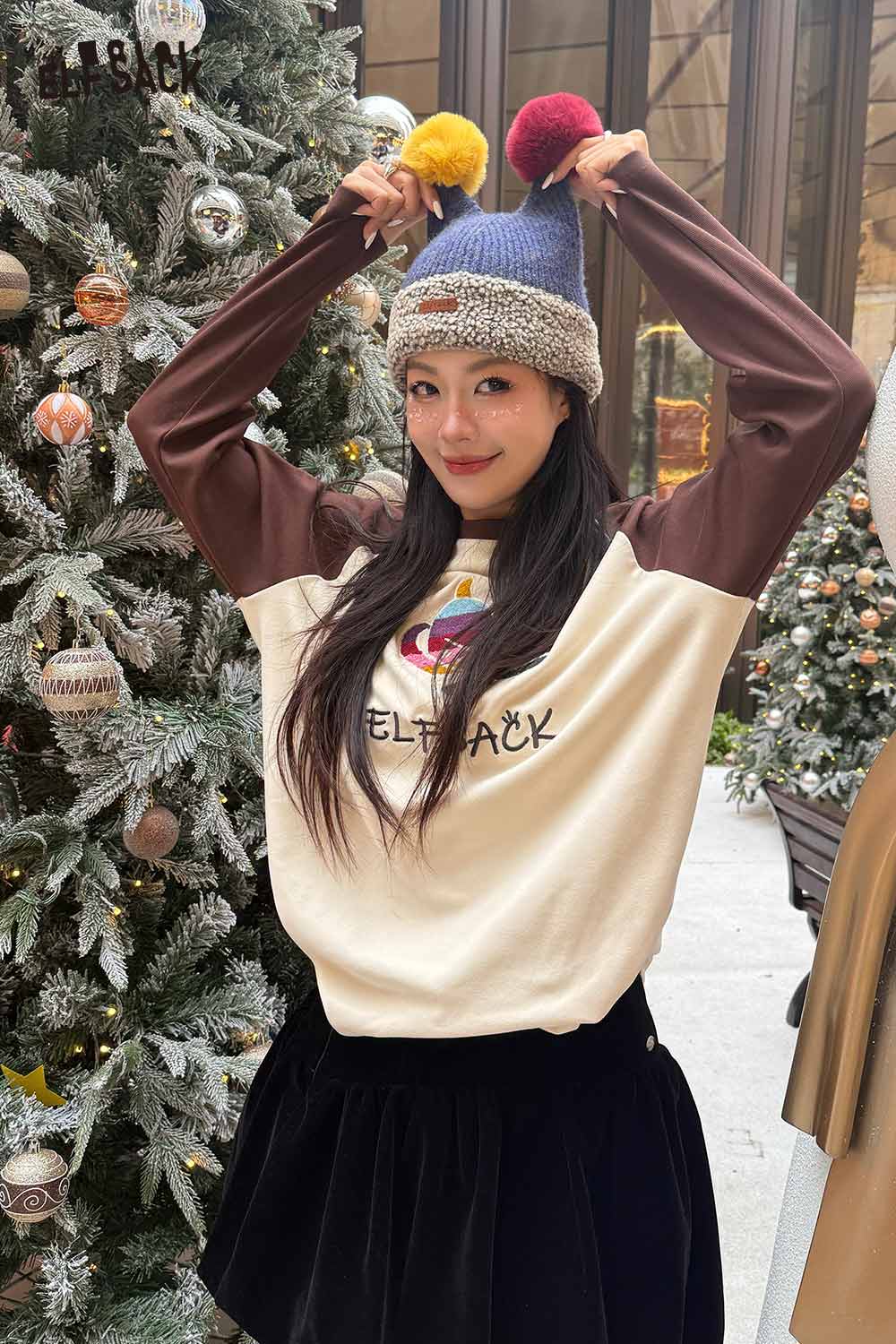 Woman wearing colorful pom pom knit beanie with playful design, posing in a festive setting