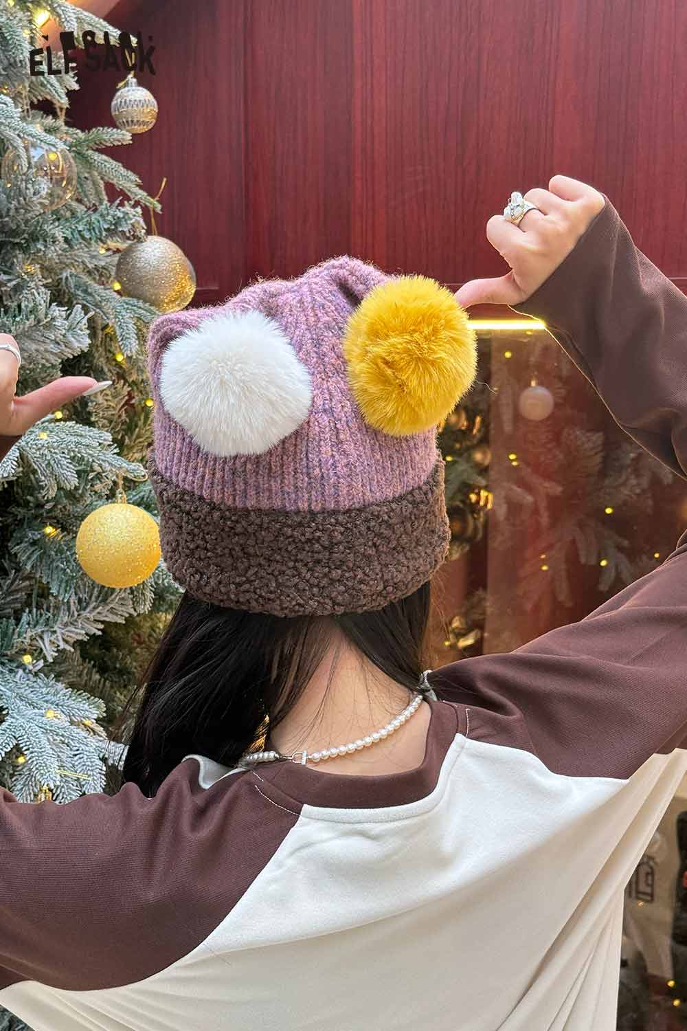 Back view of a woman wearing an ELFSACK colorful pom pom knit beanie with yellow and white fluffy pom poms