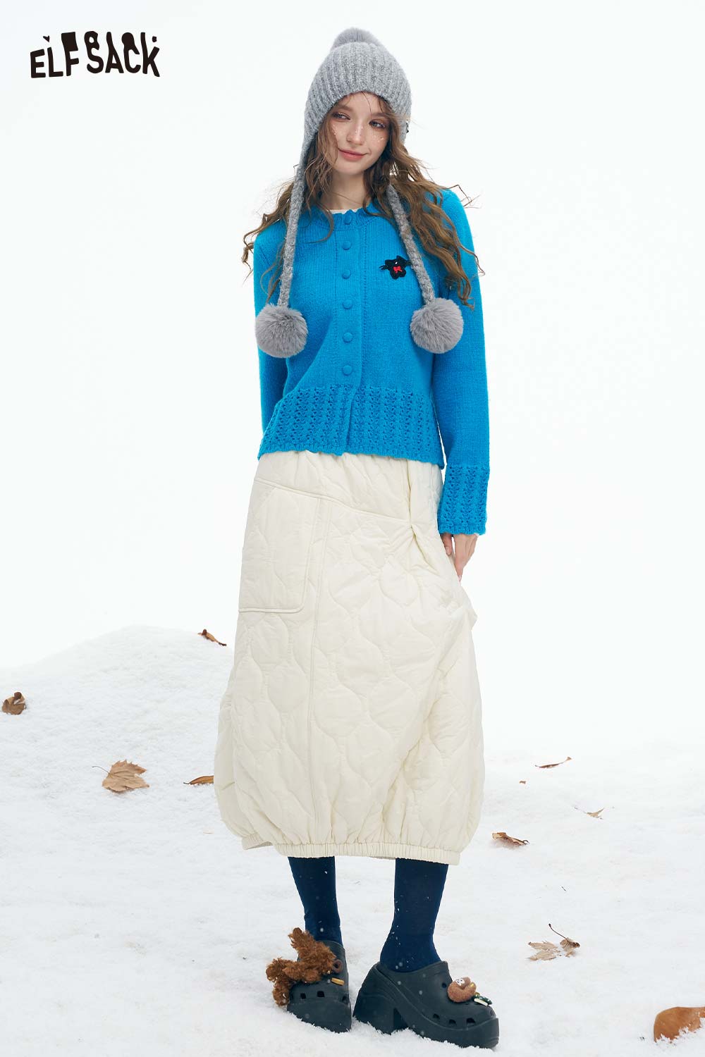 Cute knit embroidered sweater for women in blue with buttons and pom-poms, styled with a quilted skirt
