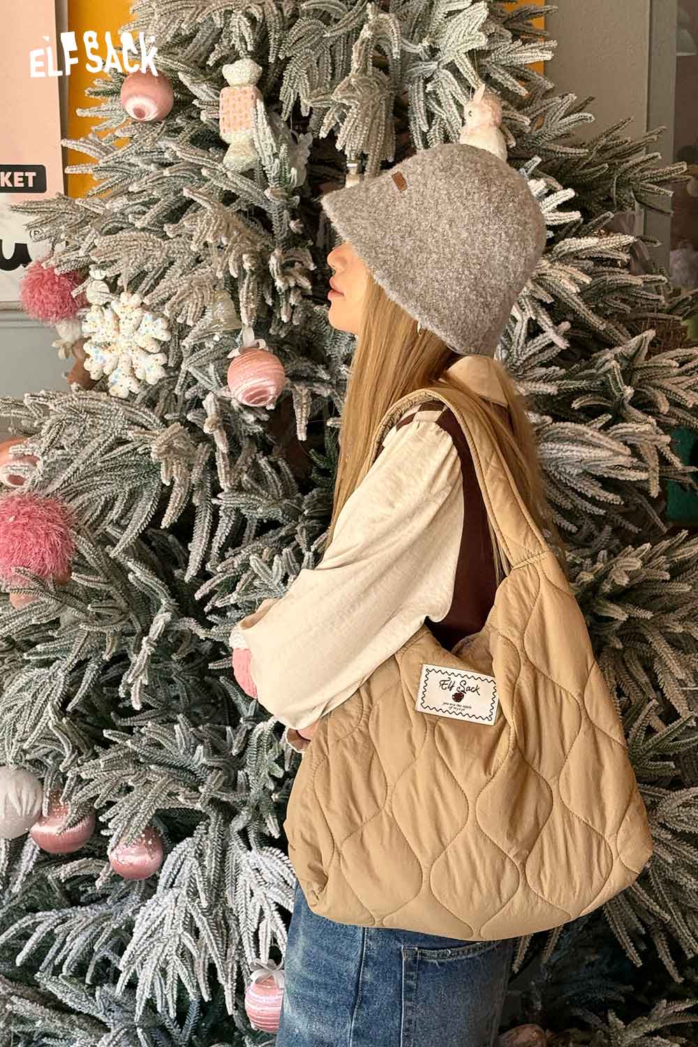 Woman wearing a soft wool knit bucket hat and carrying a quilted bag near a decorated Christmas tree