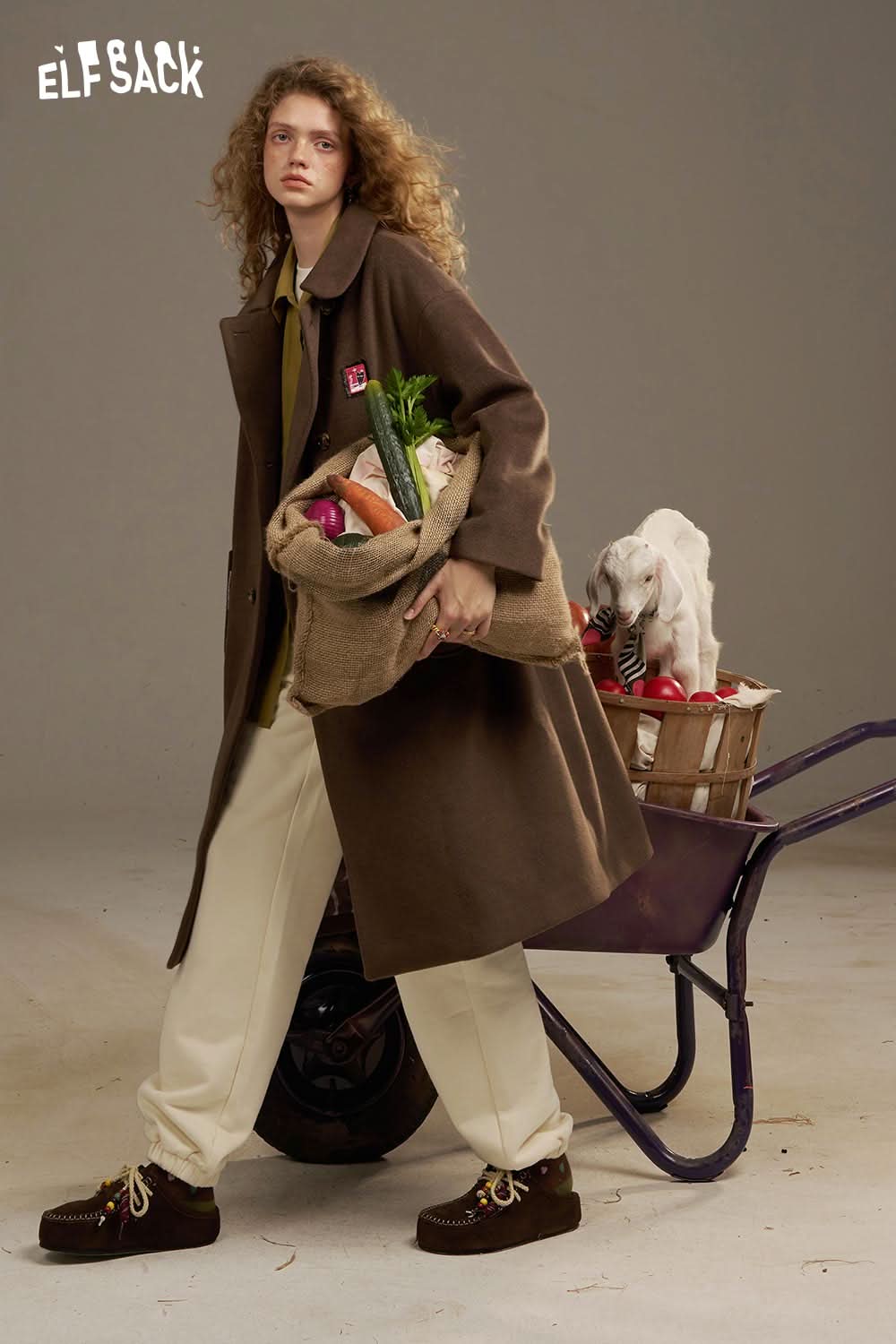 Stylish model wearing ELFSACK white cropped sweat pants for women with a brown coat and carrying a bag of groceries