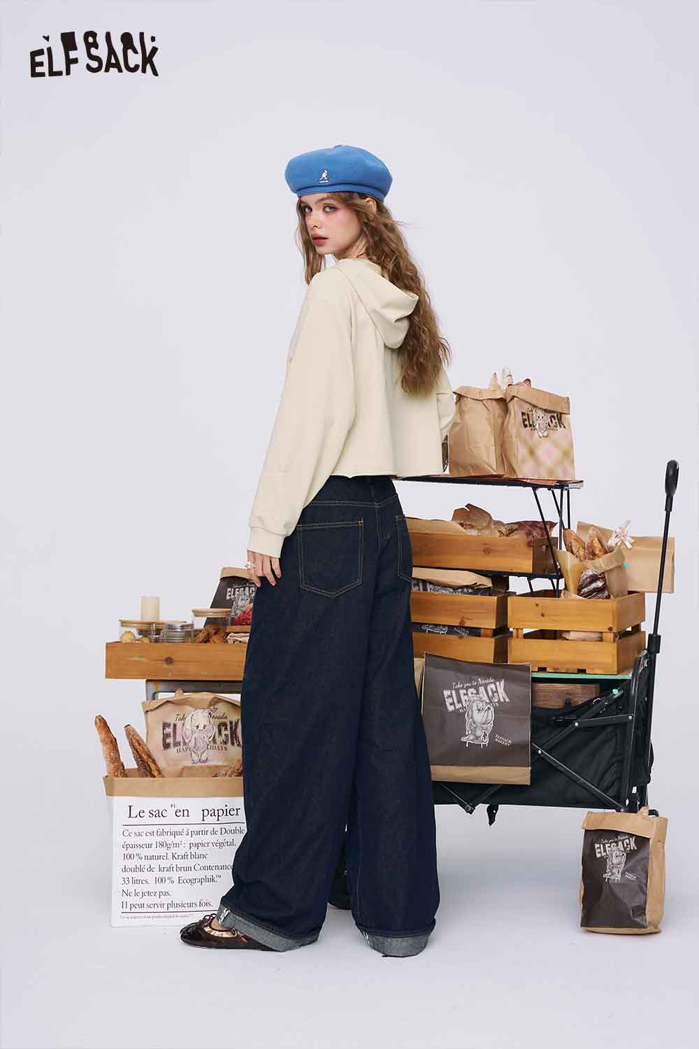 
                  
                    ELFSACK model wearing cream cropped hoodie with hood and wide leg jeans beside market cart American style print hoodie for women
                  
                
