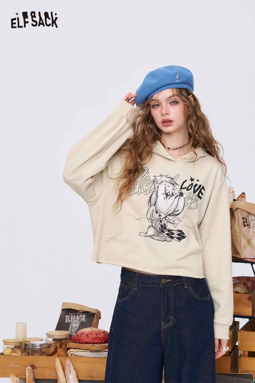 
                  
                    ELFSACK model in beige cropped American style print hoodie for women. Cartoon eagle graphic with blue beret
                  
                