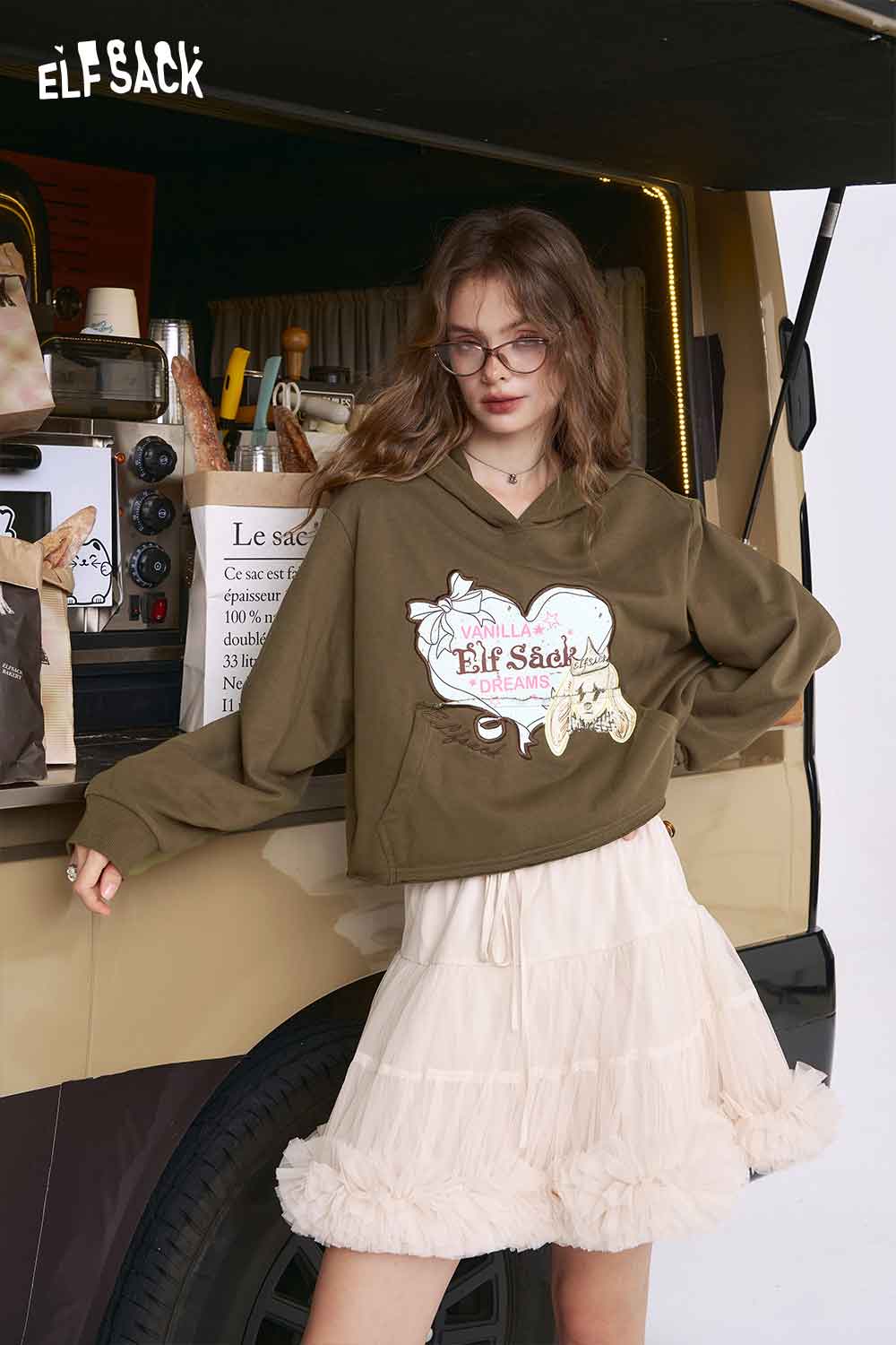 ELFSACK model wearing olive green American style print hoodie for women with ruffle cream skirt at van