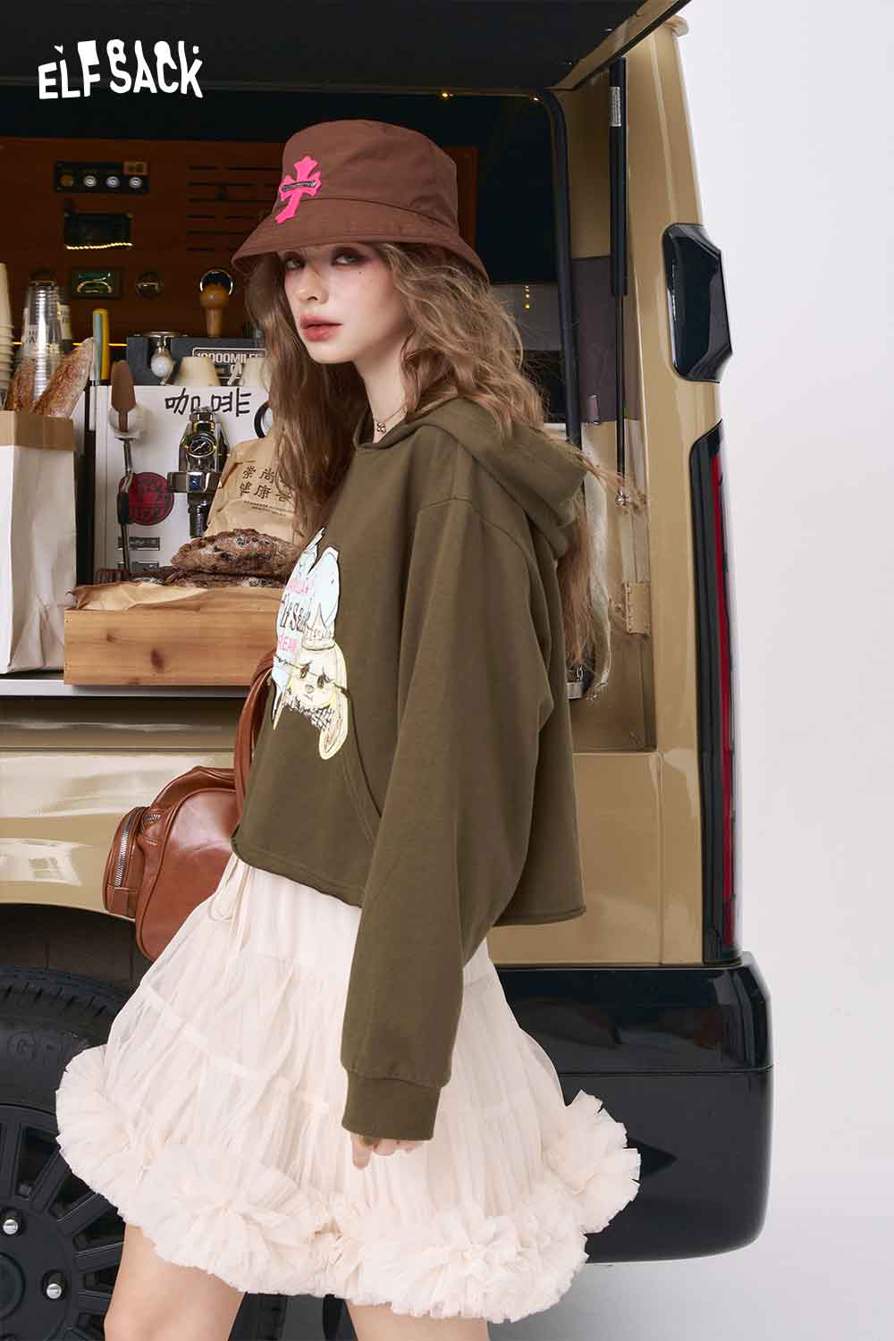 American style print hoodie for women worn by model in olive cropped hoodie with cream ruffle skirt and brown bucket hat