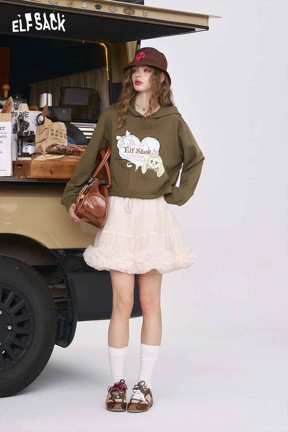 Model wearing ELFSACK American style print hoodie for women in olive green with ruffled cream skirt