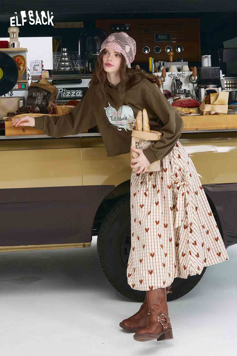 
                  
                    ELFSACK brown cropped American style print hoodie for women styled with patterned skirt and boots
                  
                