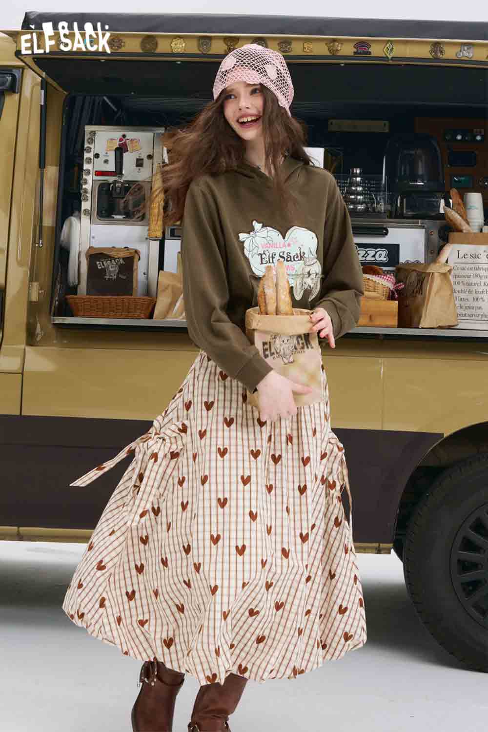 Woman wearing ELFSACK olive hoodie and striped heart skirt holding baguettes by food truck American style print hoodie for women