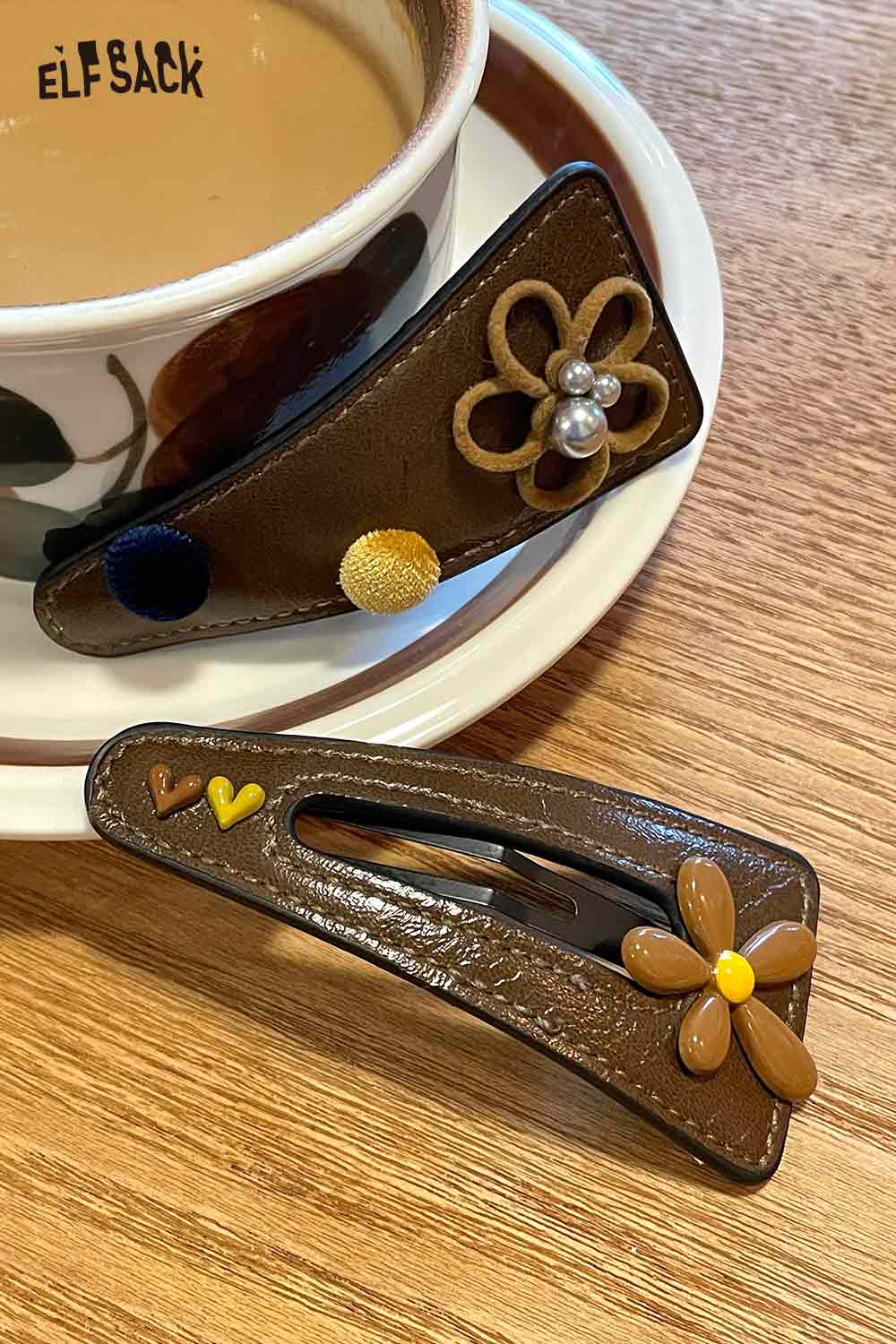 ELFSACK floral hair clip accessory with colorful decorations on a brown background next to a coffee cup