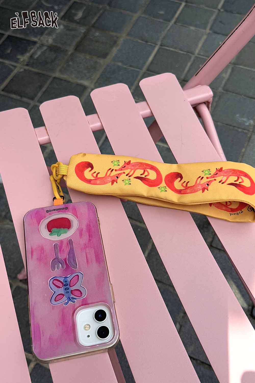 Yellow ELFSACK fox character phone strap with playful design on a pink table