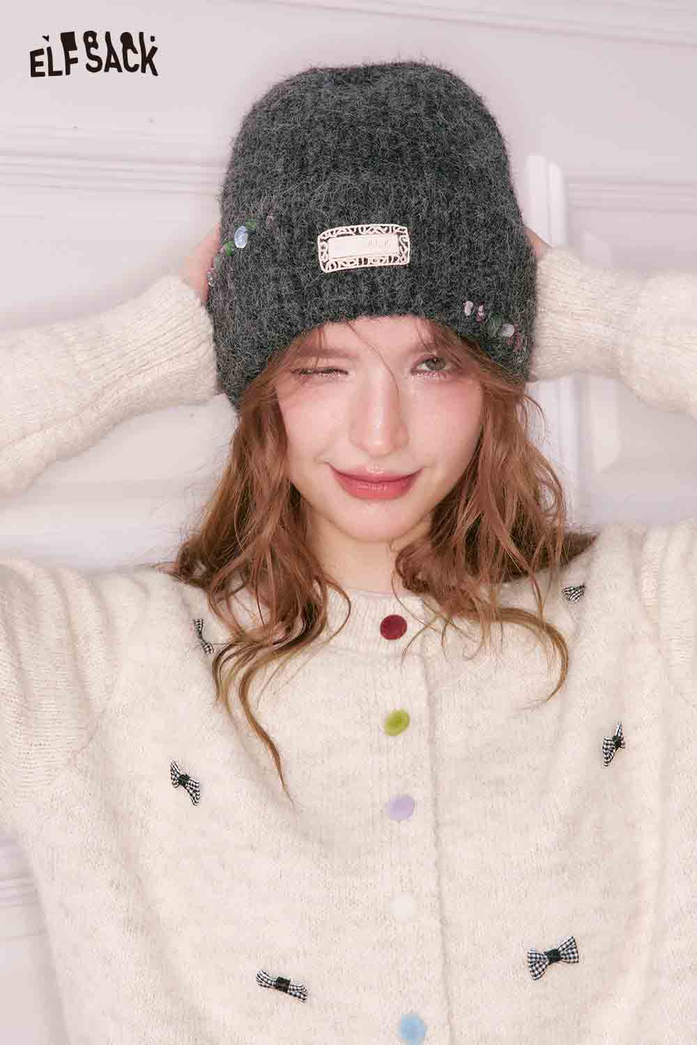 ELFSACK girly bow cardigan in cream with colorful bow details, paired with a cozy gray beanie