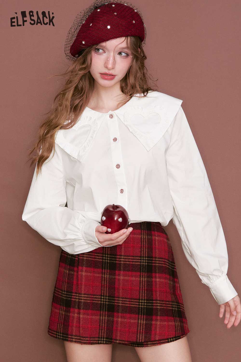 ELFSACK heart collar blouse for women in white paired with a plaid skirt, model holding an apple