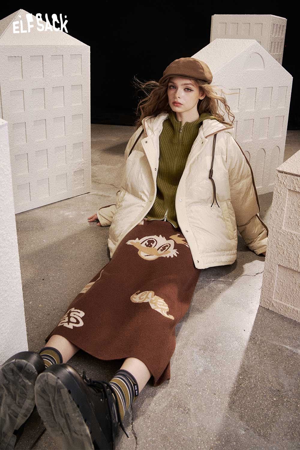 Model wearing heart print knit sweater styled with a winter coat and a patterned skirt