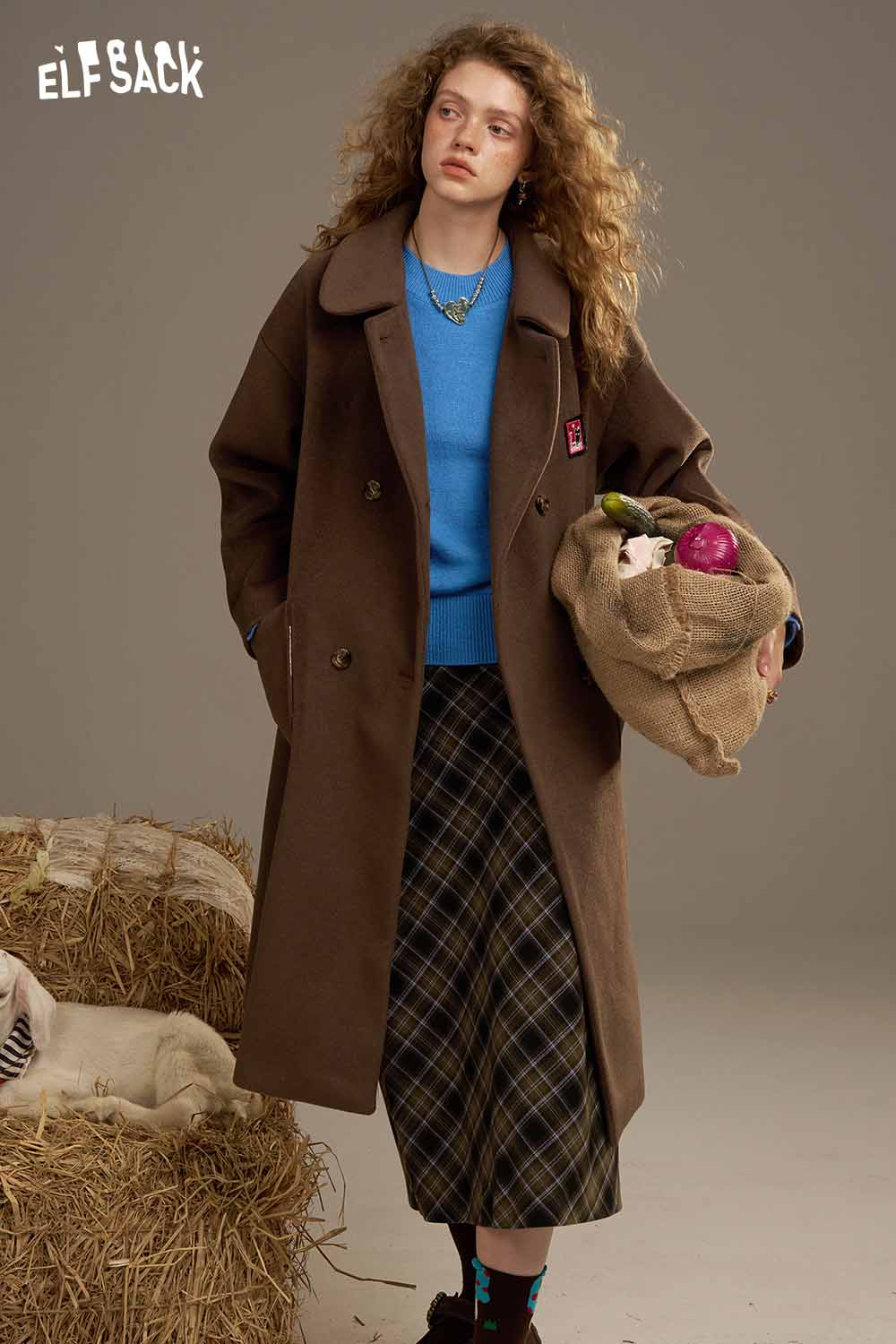 Model wearing a lantern sleeve fitted knitted sweater styled with a brown coat and plaid skirt
