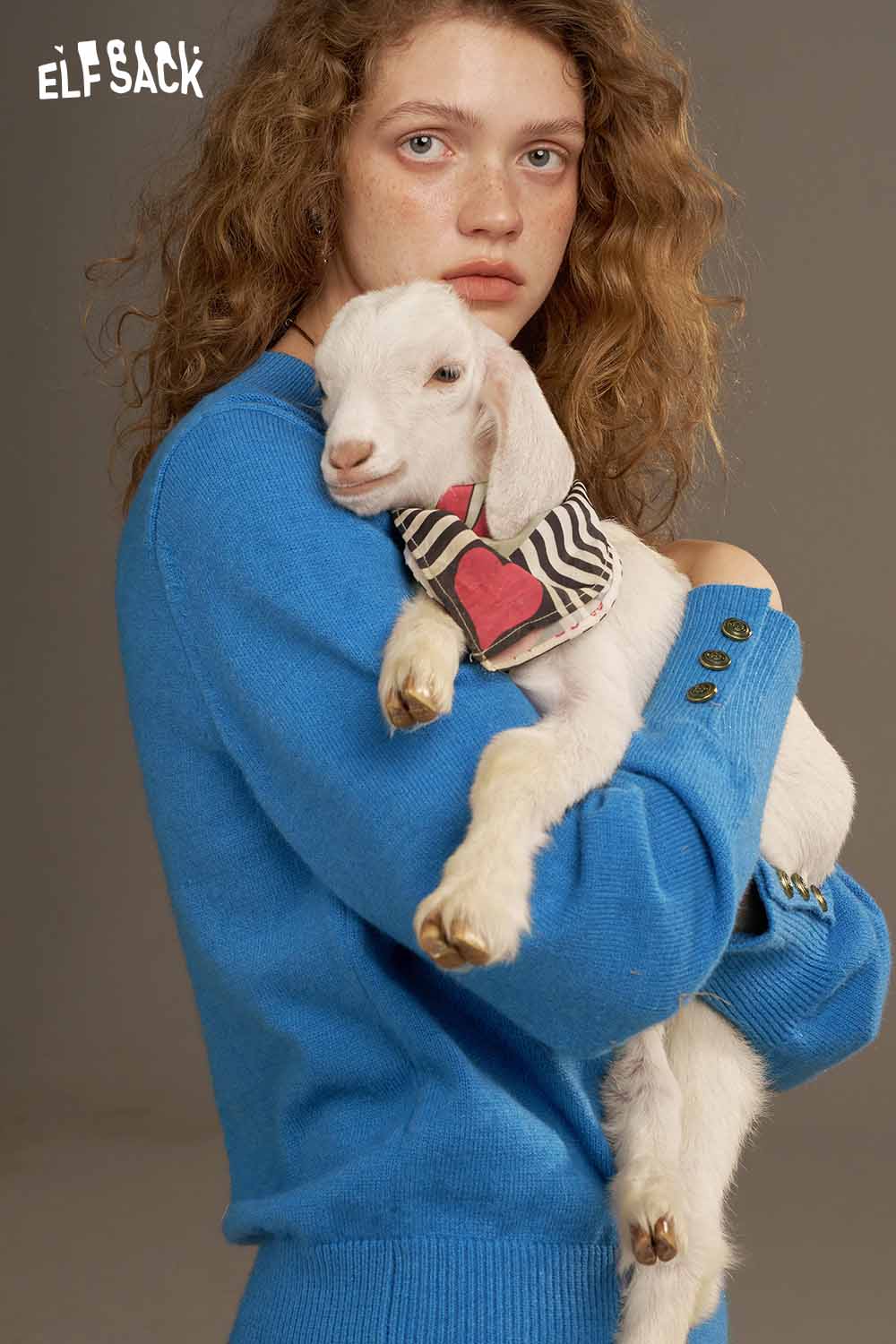 Model wearing an ELFSACK lantern sleeve fitted knitted sweater in blue while holding a small goat