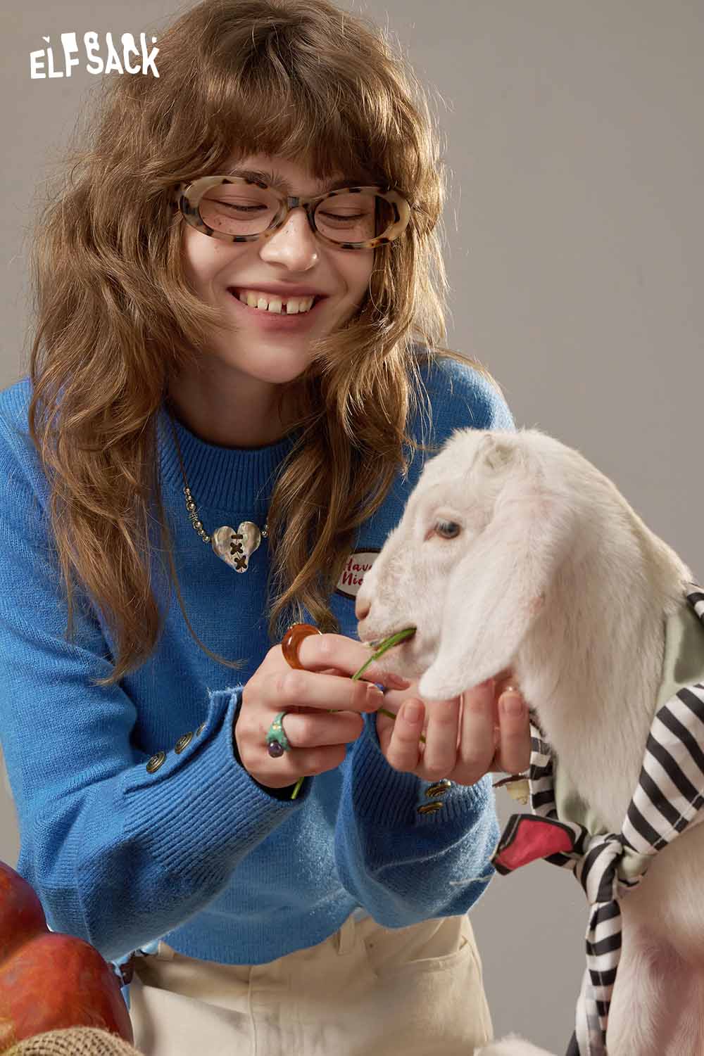 ELFSACK lantern sleeve fitted knitted sweater in bright blue, worn by a smiling model holding a goat.