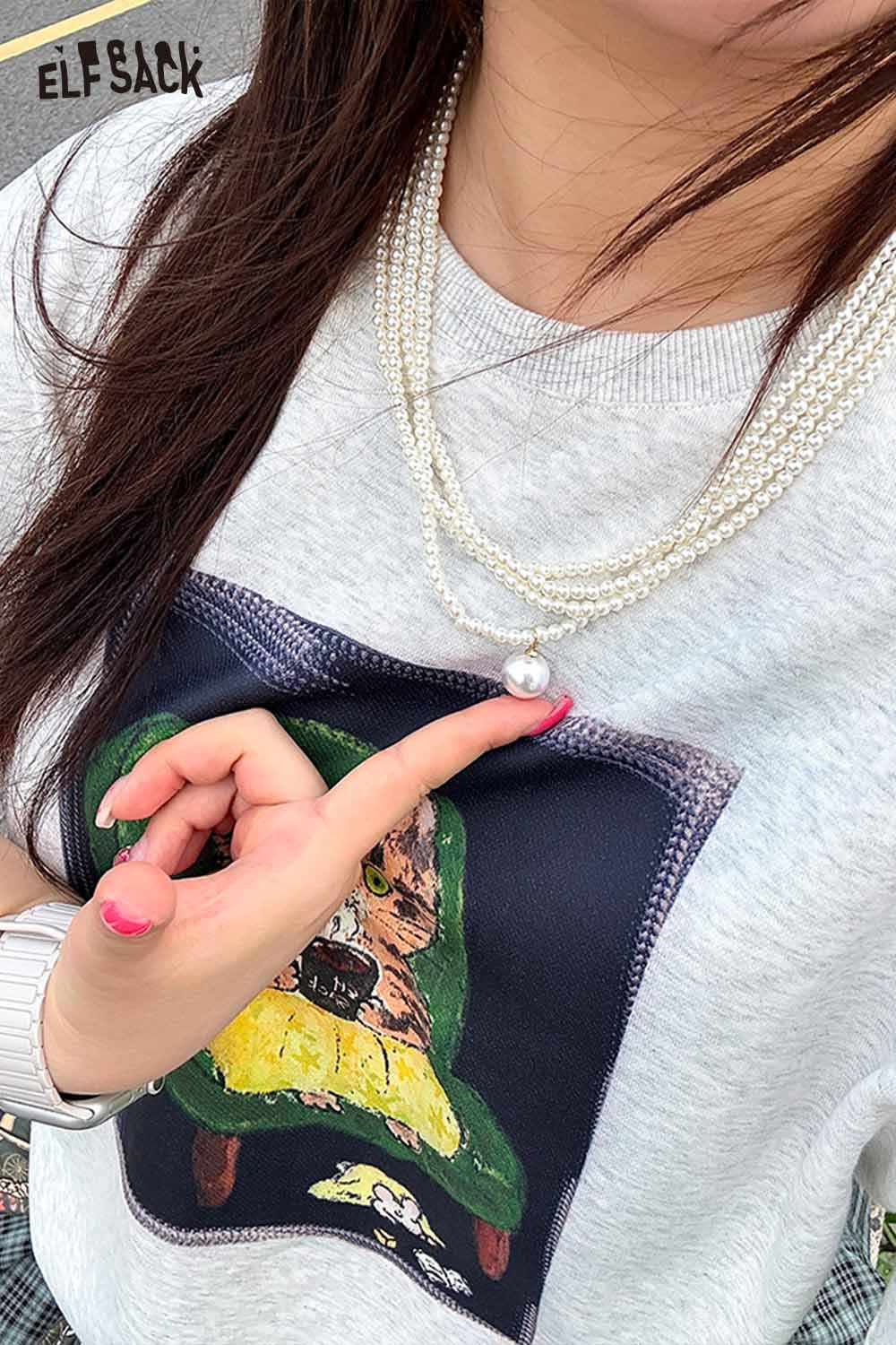 Layered pearl choker necklace worn with a graphic sweatshirt, adding a touch of elegance.