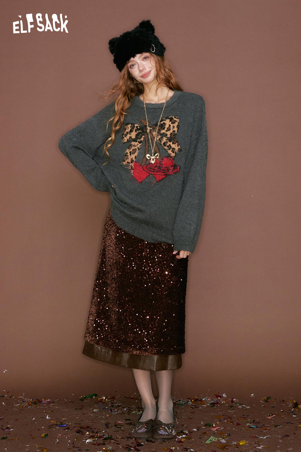 ELFSACK leopard print graphic sweater in gray with festive bow design, styled with a sequin skirt