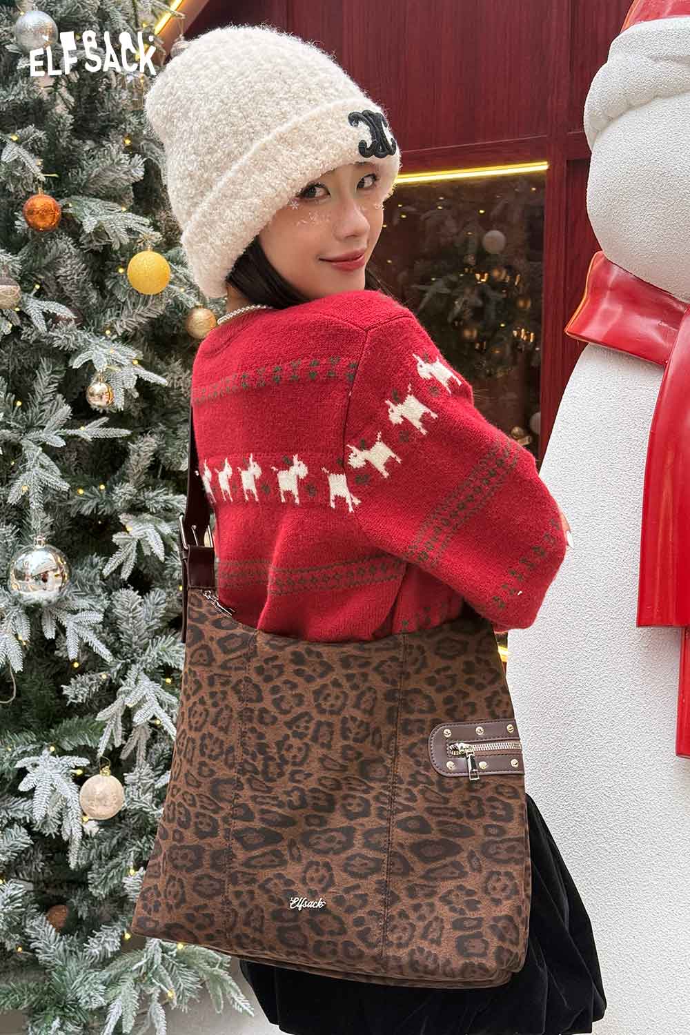 Model wearing a cozy sweater with a leopard print suede crossbody bag in a festive outdoor setting