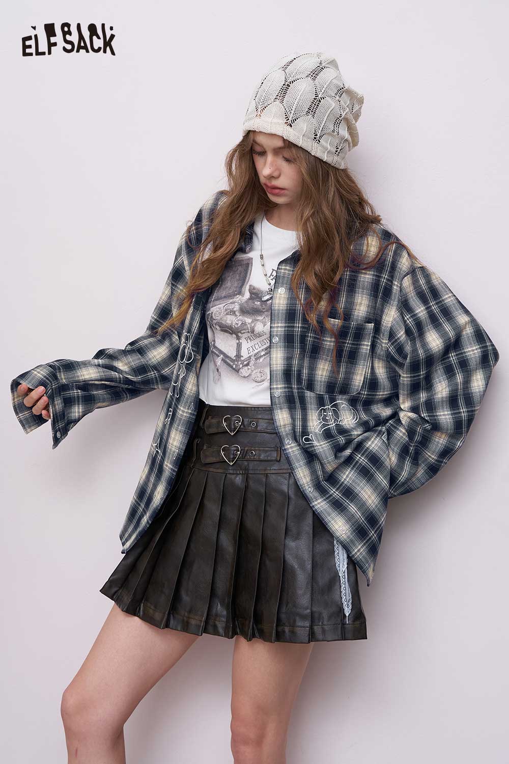 ELFSACK model wearing women's dark blue plaid graphic shirt layered over a white tee with black pleated leather skirt