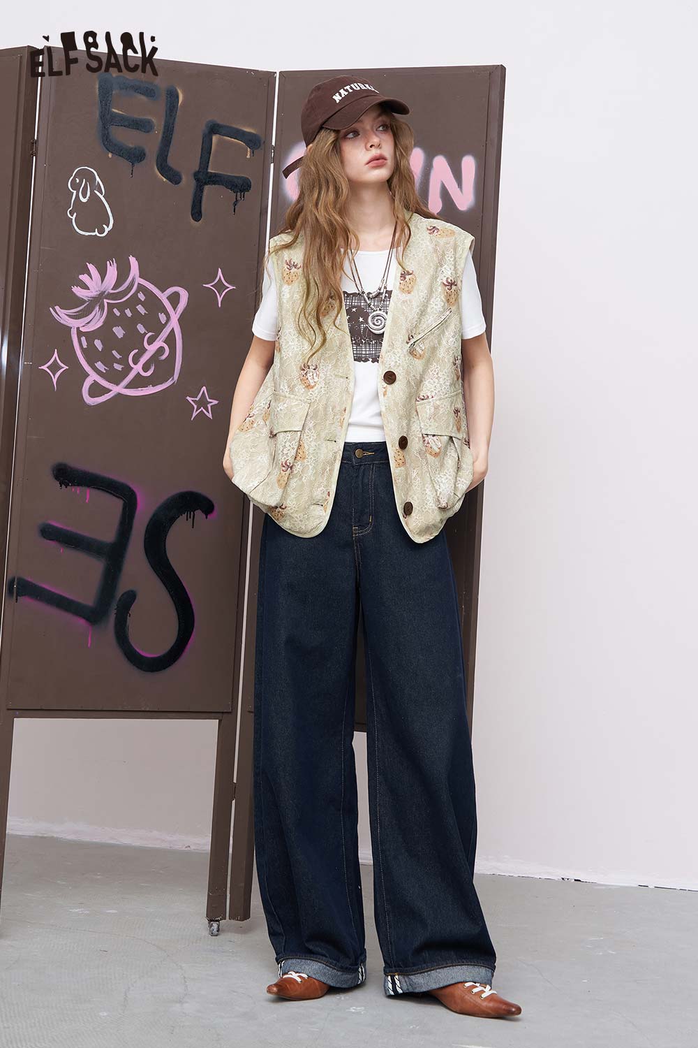 ELFSACK women's graphic lace vest layered over graphic tee with embroidered details paired with wide leg jeans and cap