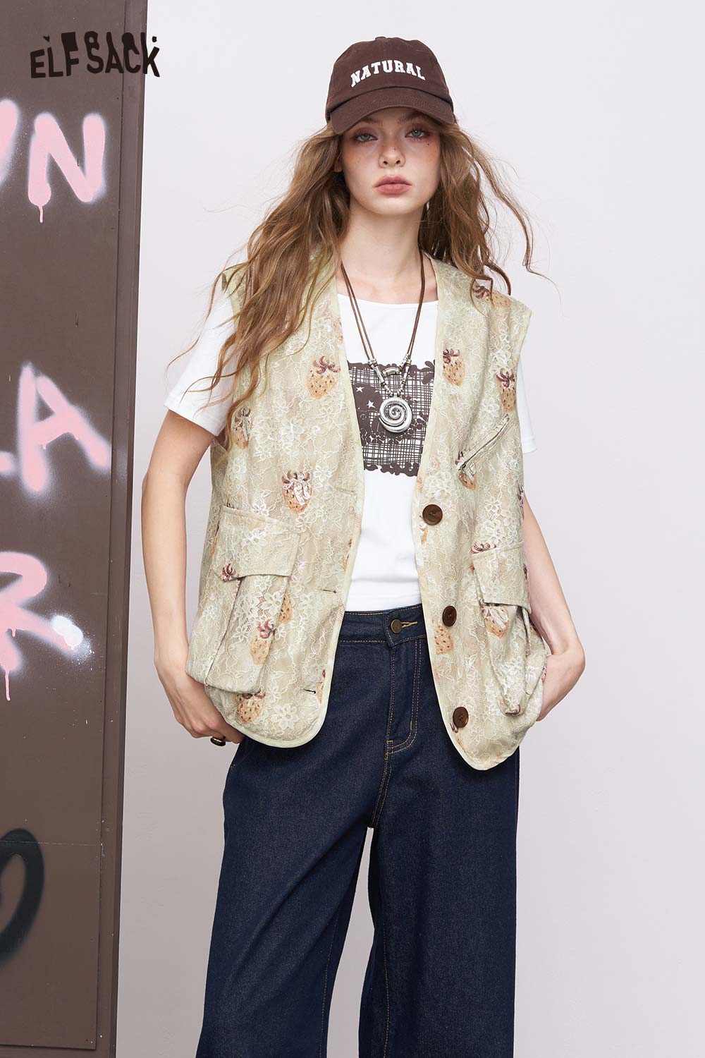 ELFSACK women's graphic lace vest in beige worn over graphic tee with wide leg jeans and brown cap