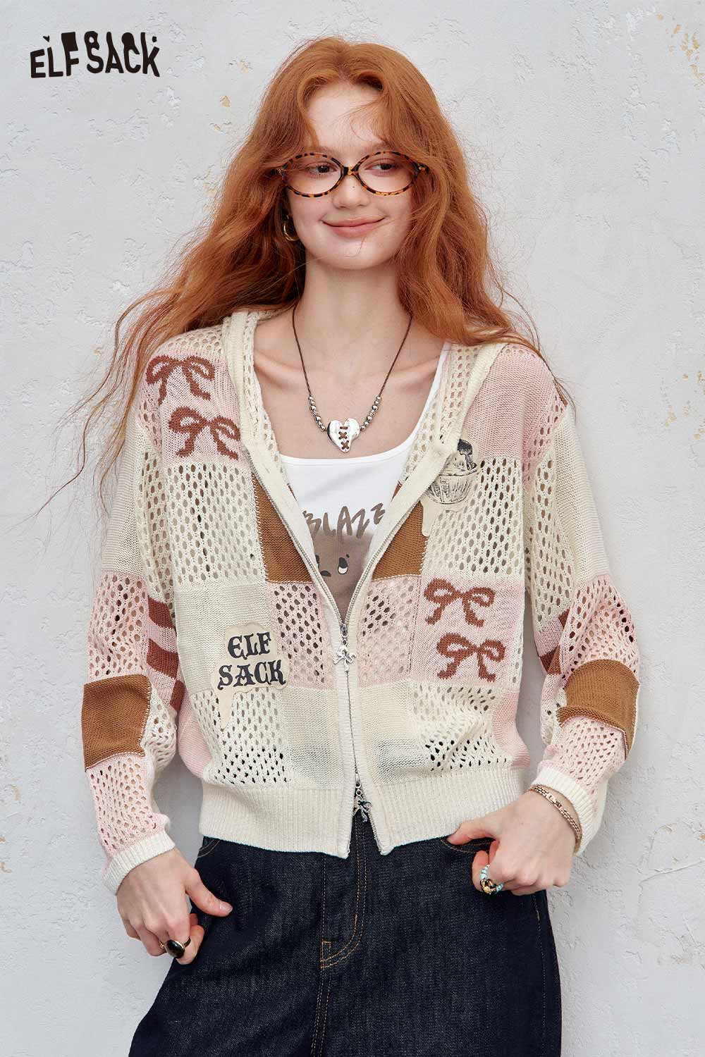 Model wearing ELFSACK women's openwork knit zip hoodie in cream and pink with bow motifs elbow patches over tank top